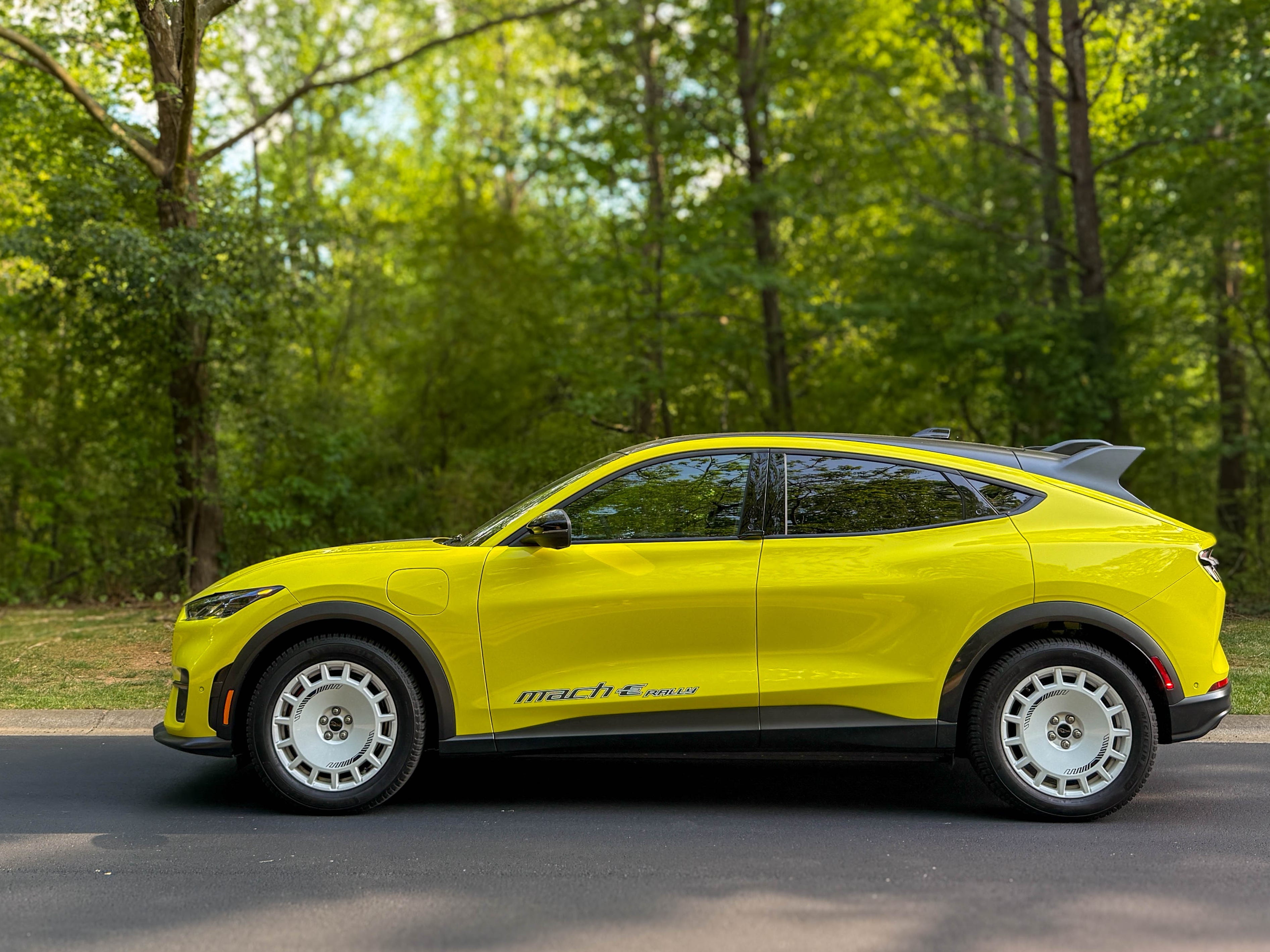 The left side of a yellow 2025 Ford Mustang Mach-E Rally EV SUV parked by the woods.