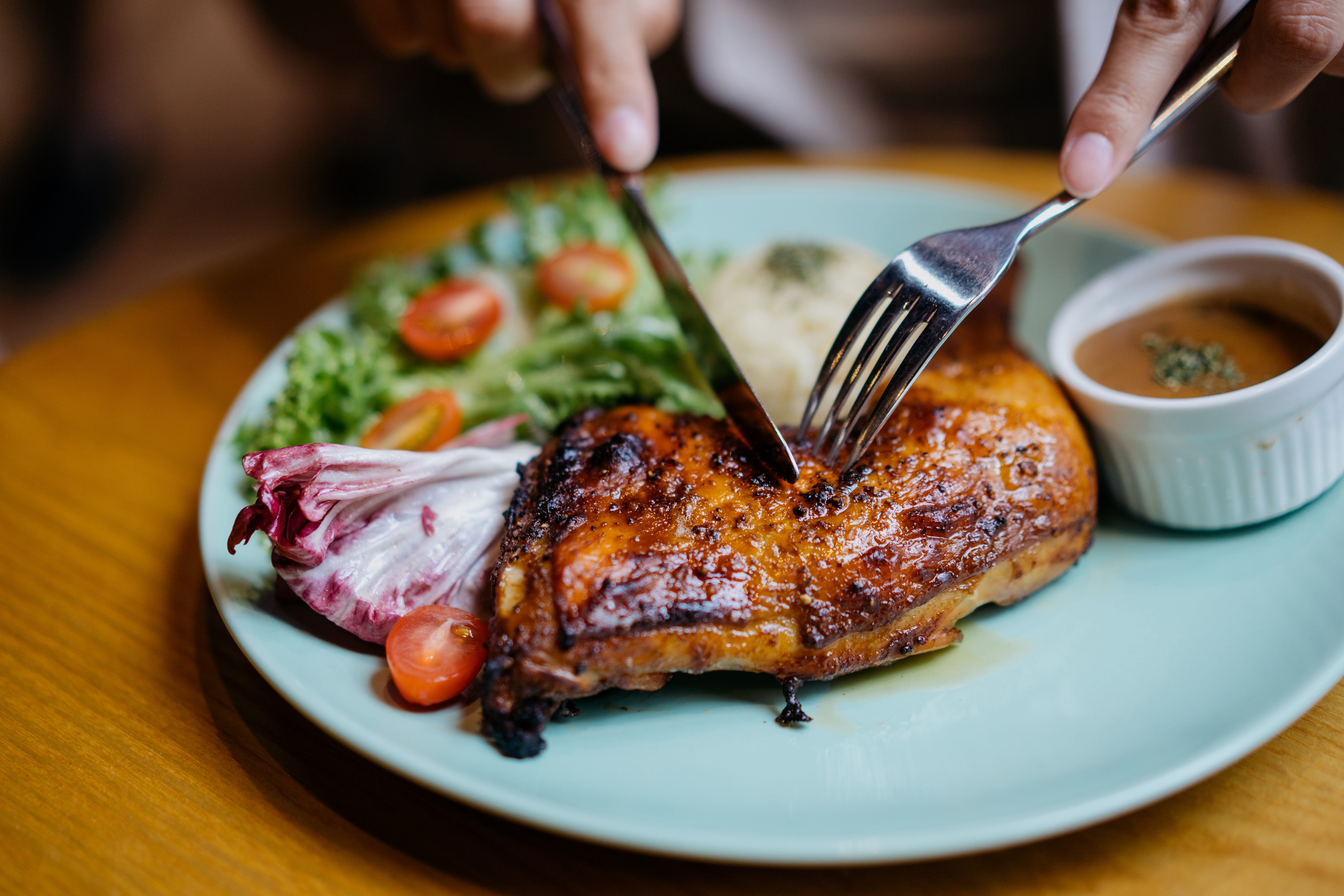 Fork and knife cutting into a piece of chicken on a plate