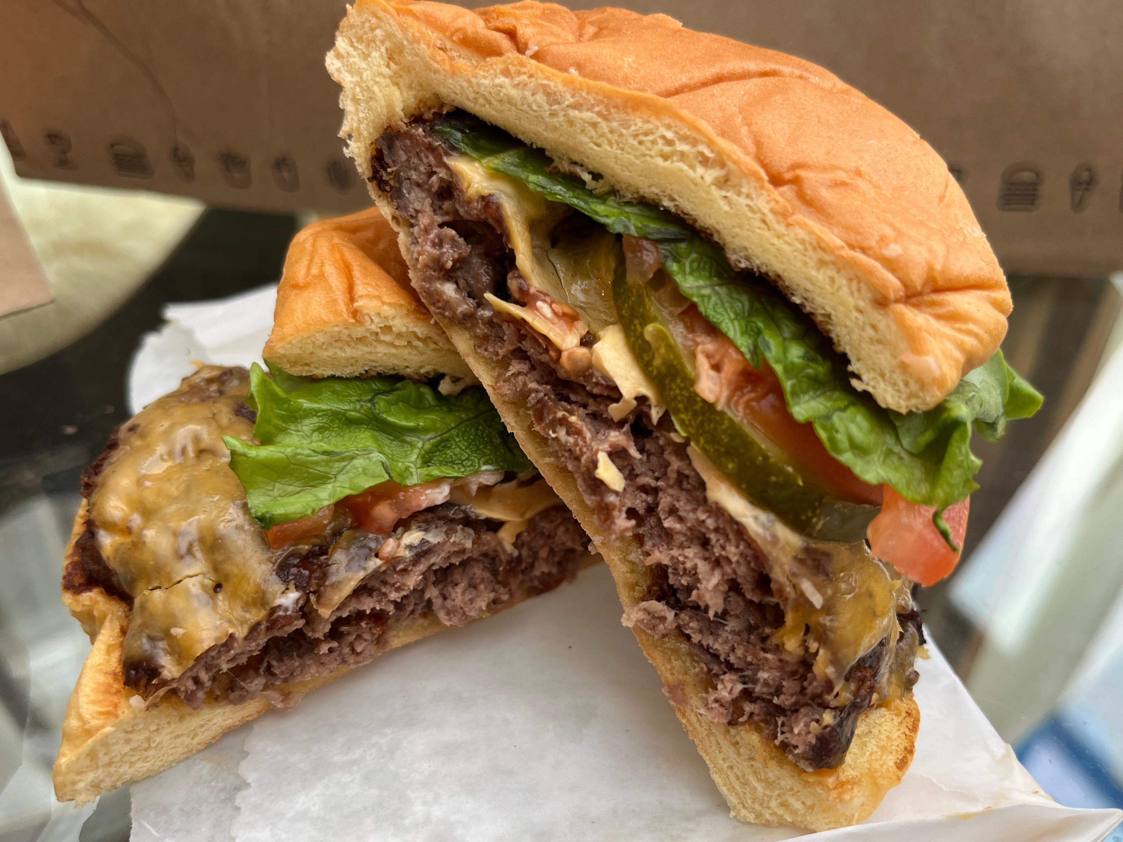 Two halves of a cheeseburger with lettuce, tomato, and pickles stacked on top of each other.