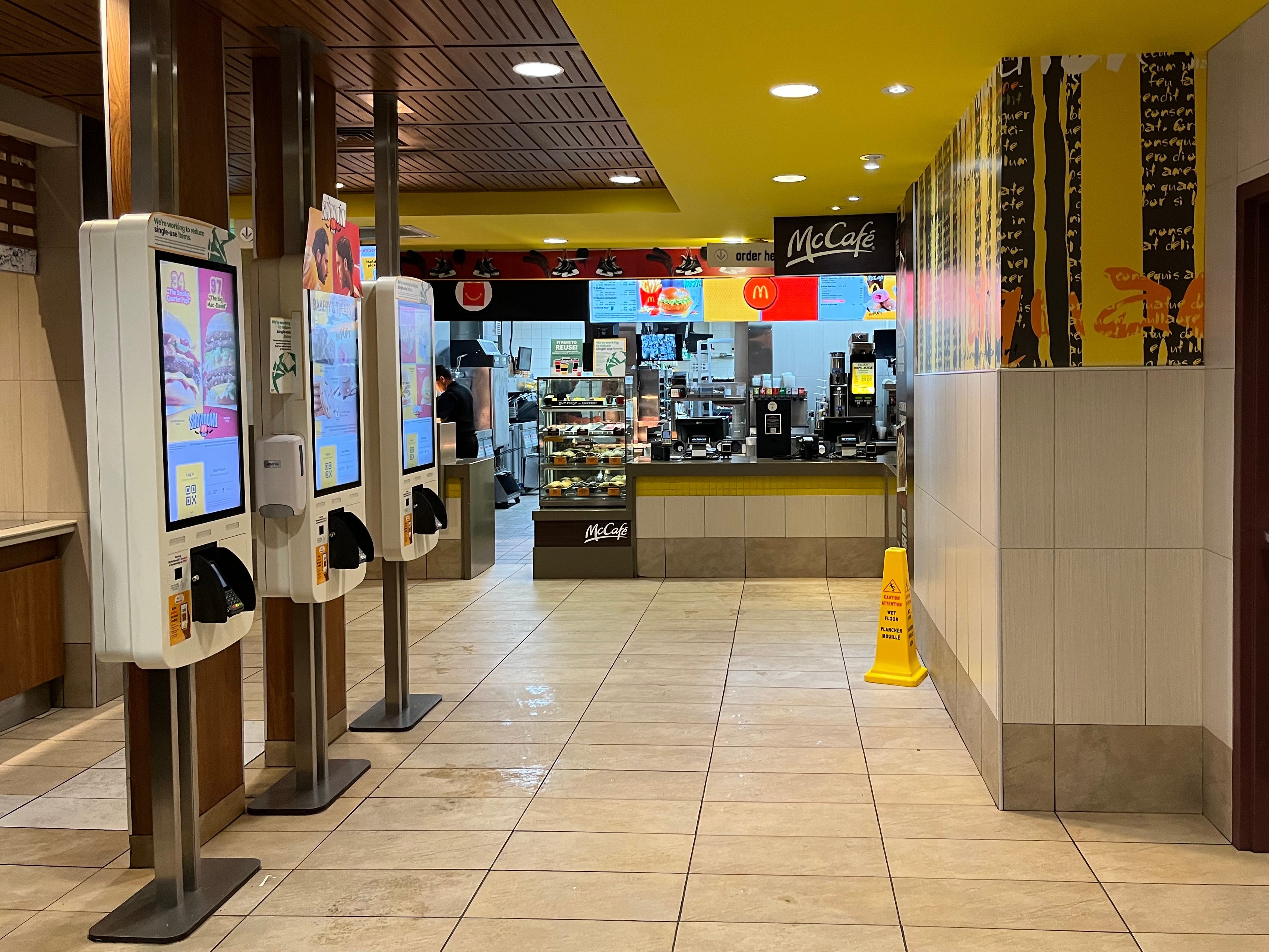 The interior of a McDonald's restaurant with three ordering Kiosks.