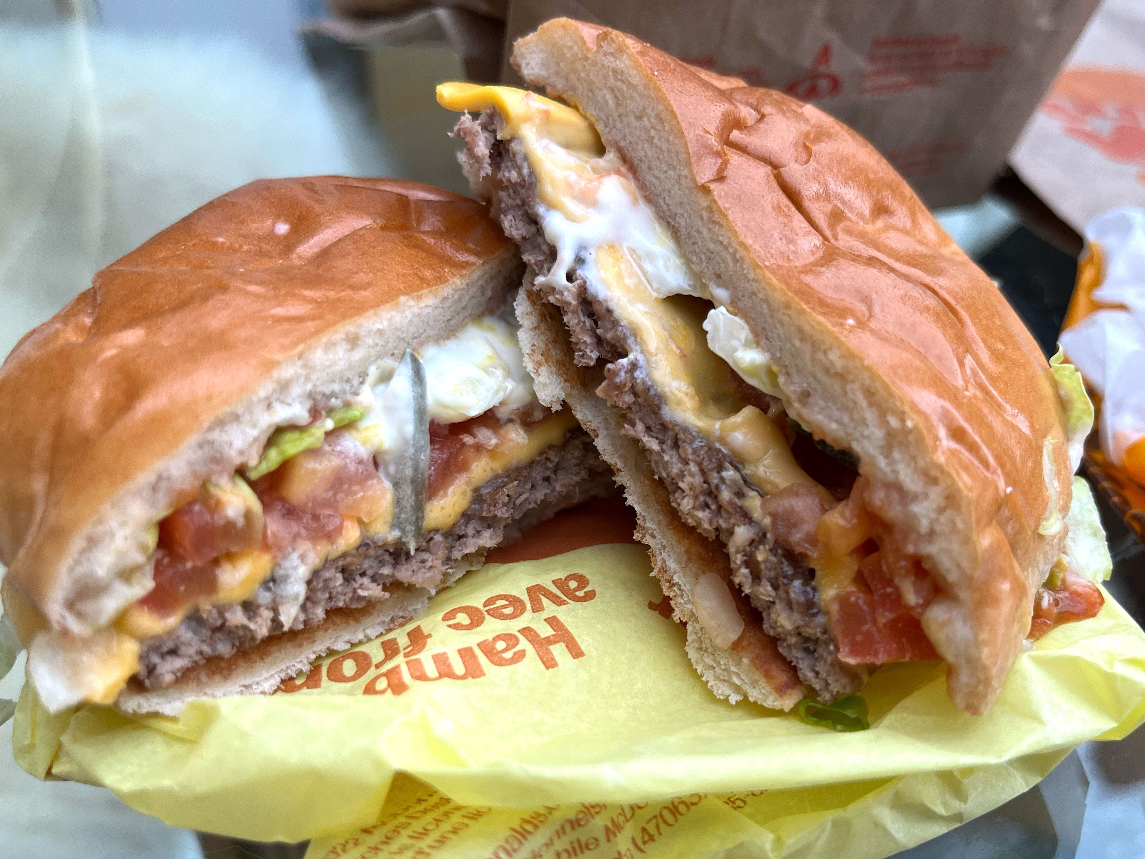 Two halves of a cheeseburger with lettuce, tomato, pickles, and mayo stacked on top of each other.