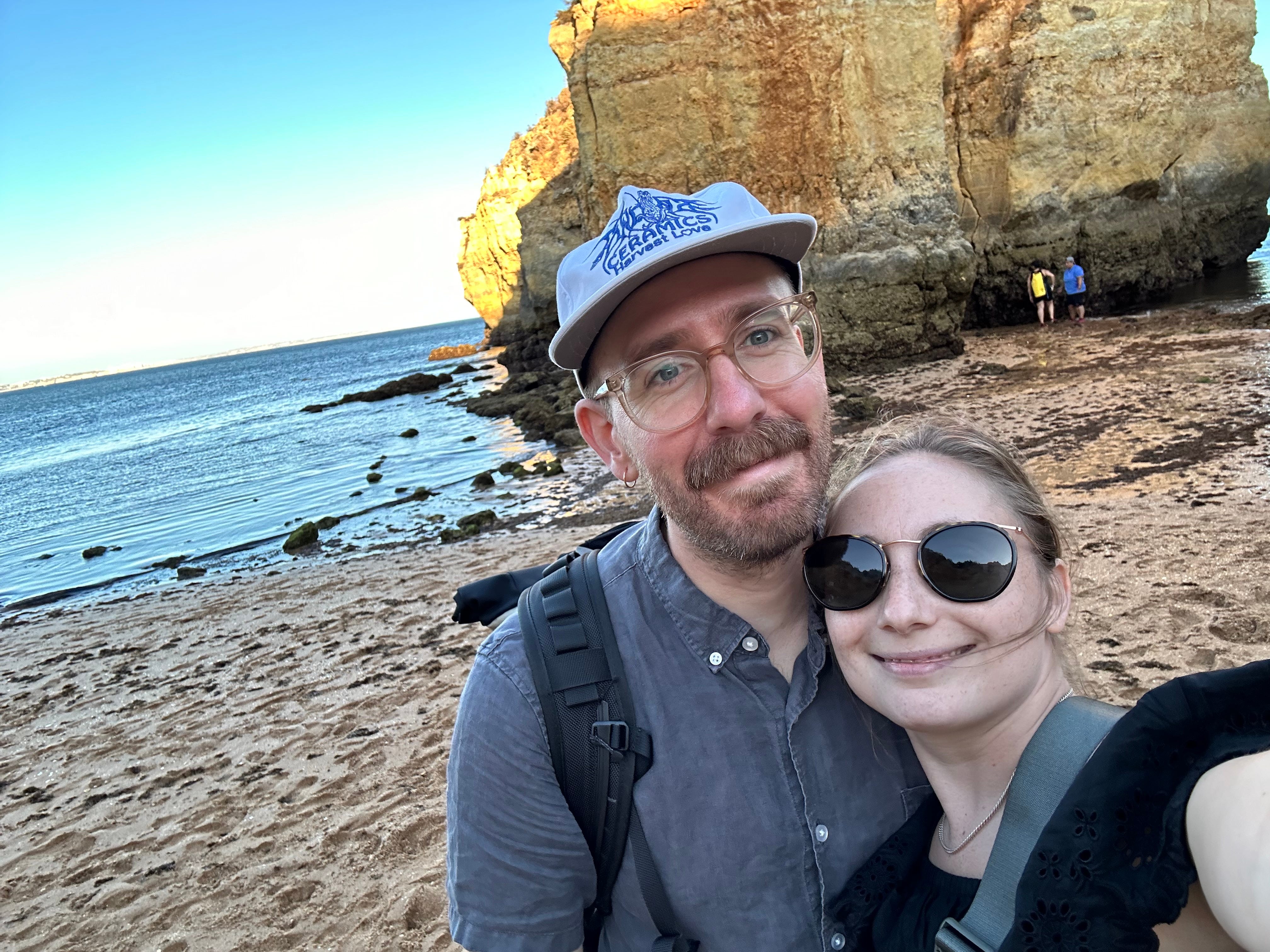 The author and her boyfriend pose on a beach in front of a large rock.