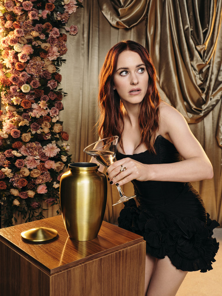 Rachel Brosnahan in a black mini dress with ruffled hem, holding a martini glass.