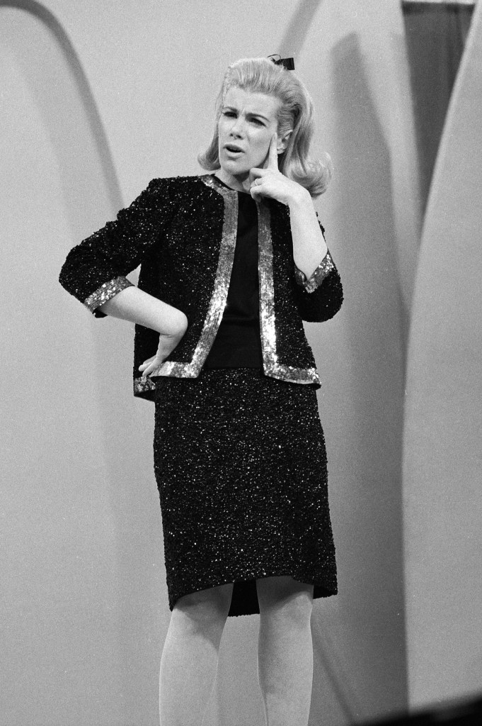 Joan Rivers in a black suit jacket with metallic trim, and a metallic black dress with her hair in a bow.