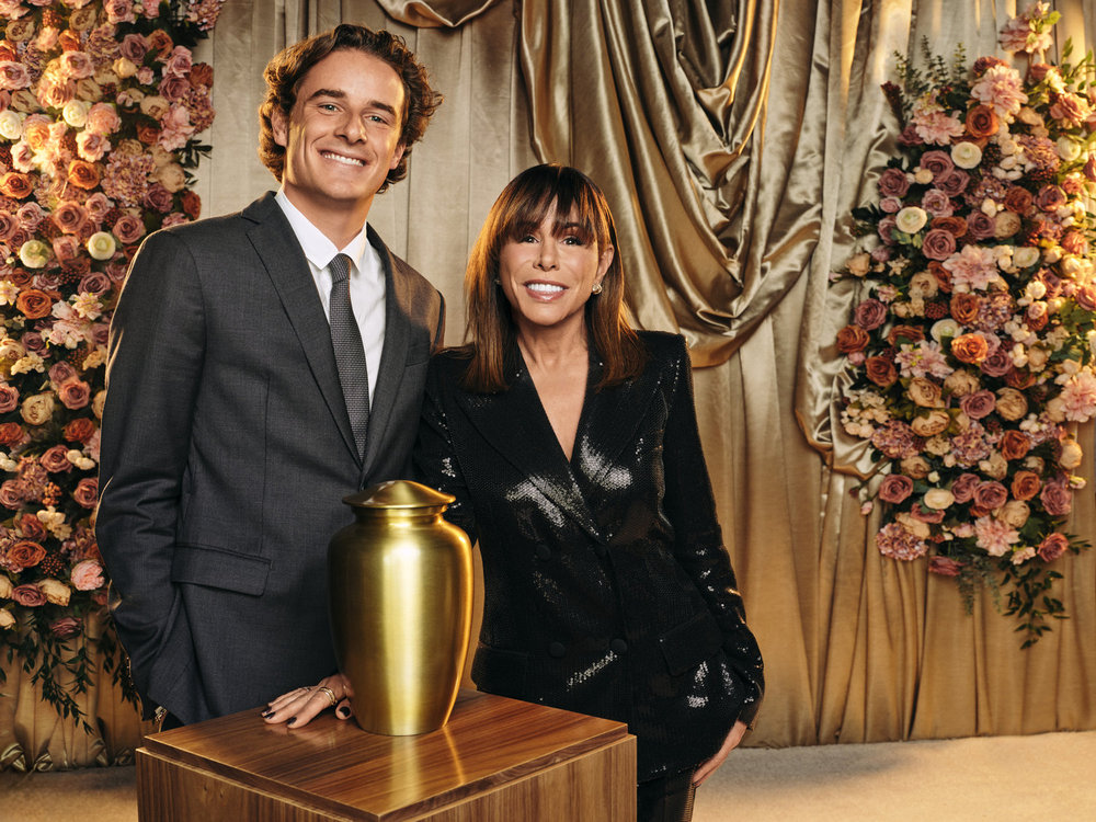 Cooper Endicott in a grey suit, grey tie and white shirt, Melissa Rivers in a shiny black suit jacket and pants.