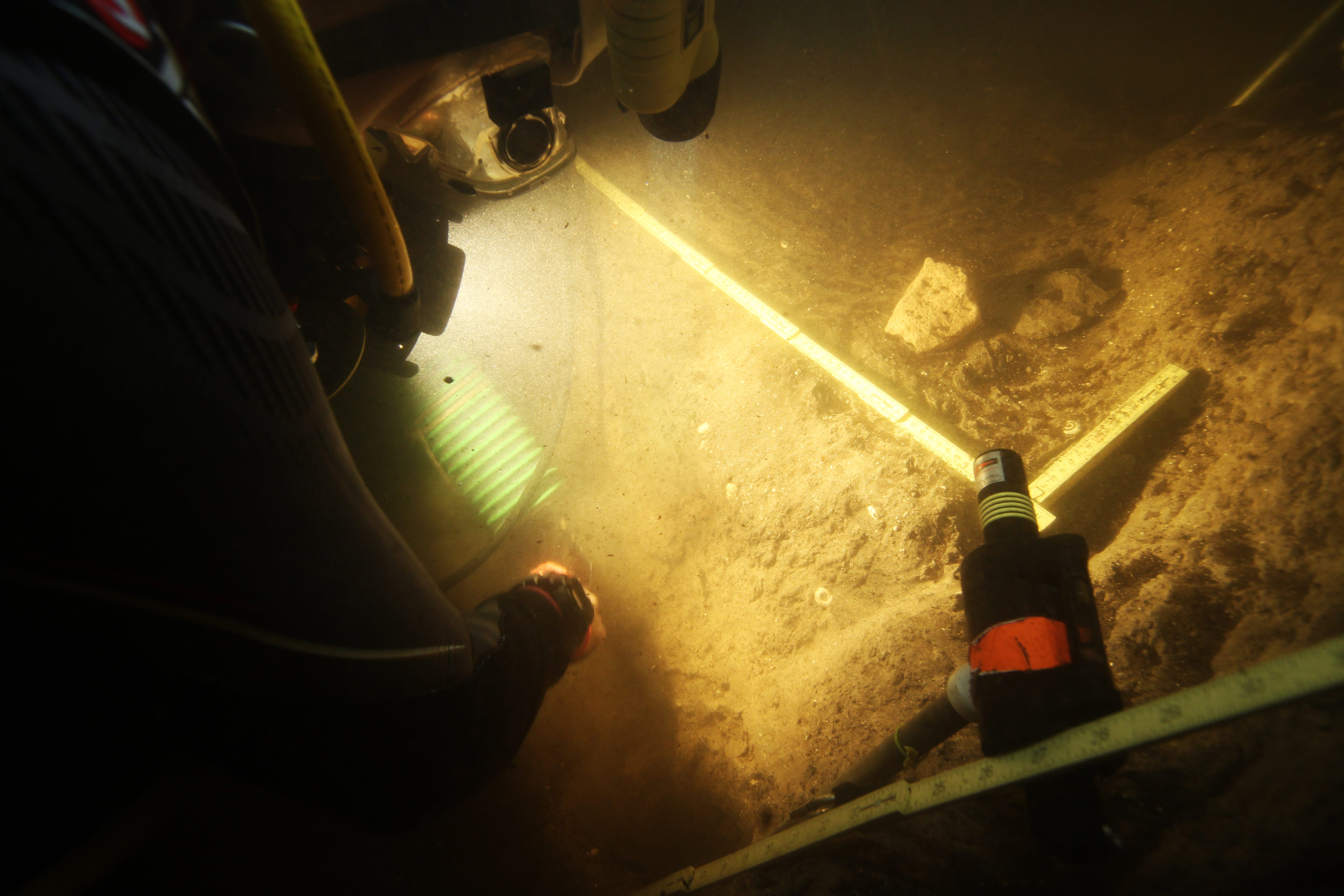 Divers hold a light underwater on a riverbed
