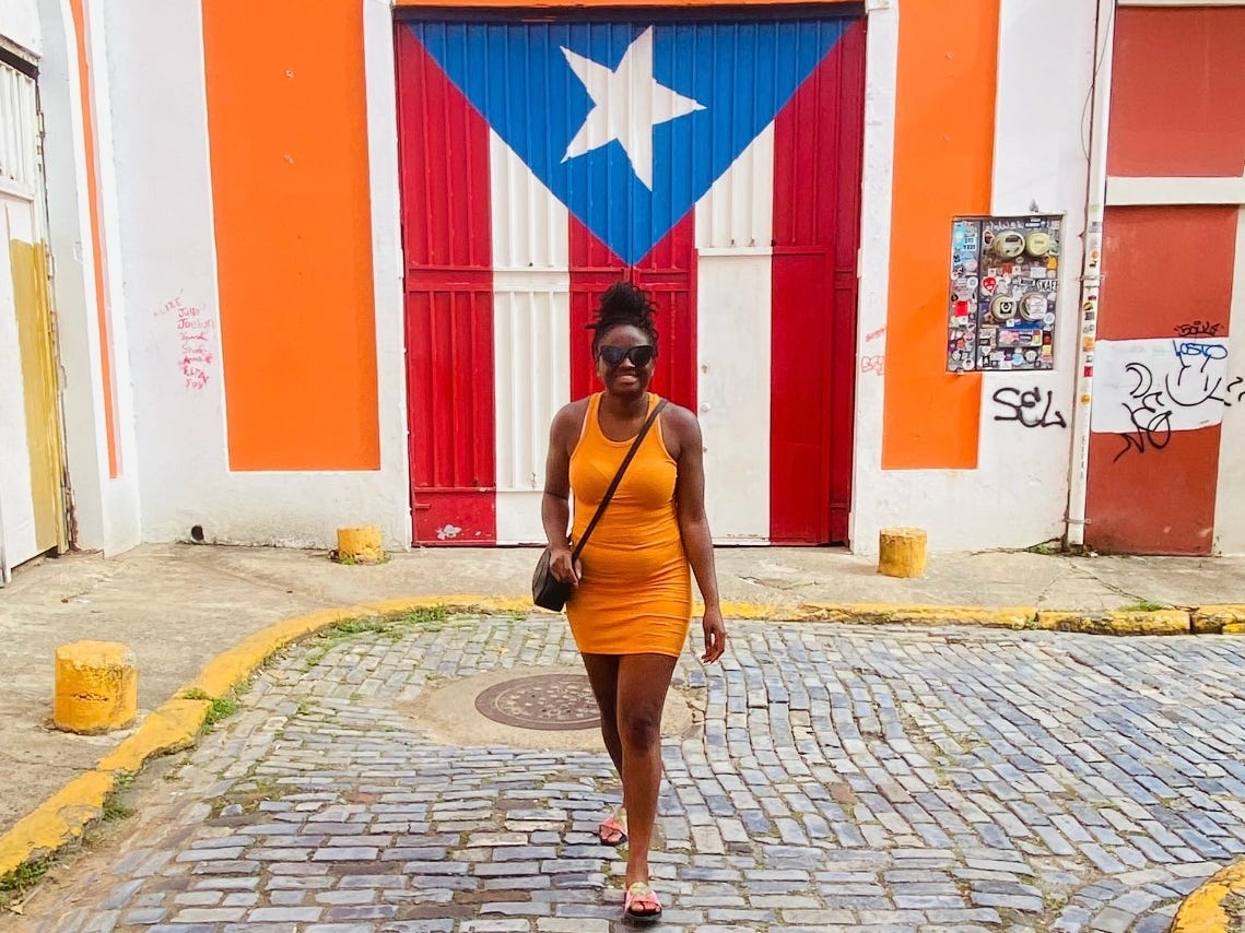 Mariette stands in front of a door painted like the Puerto Rican flag.