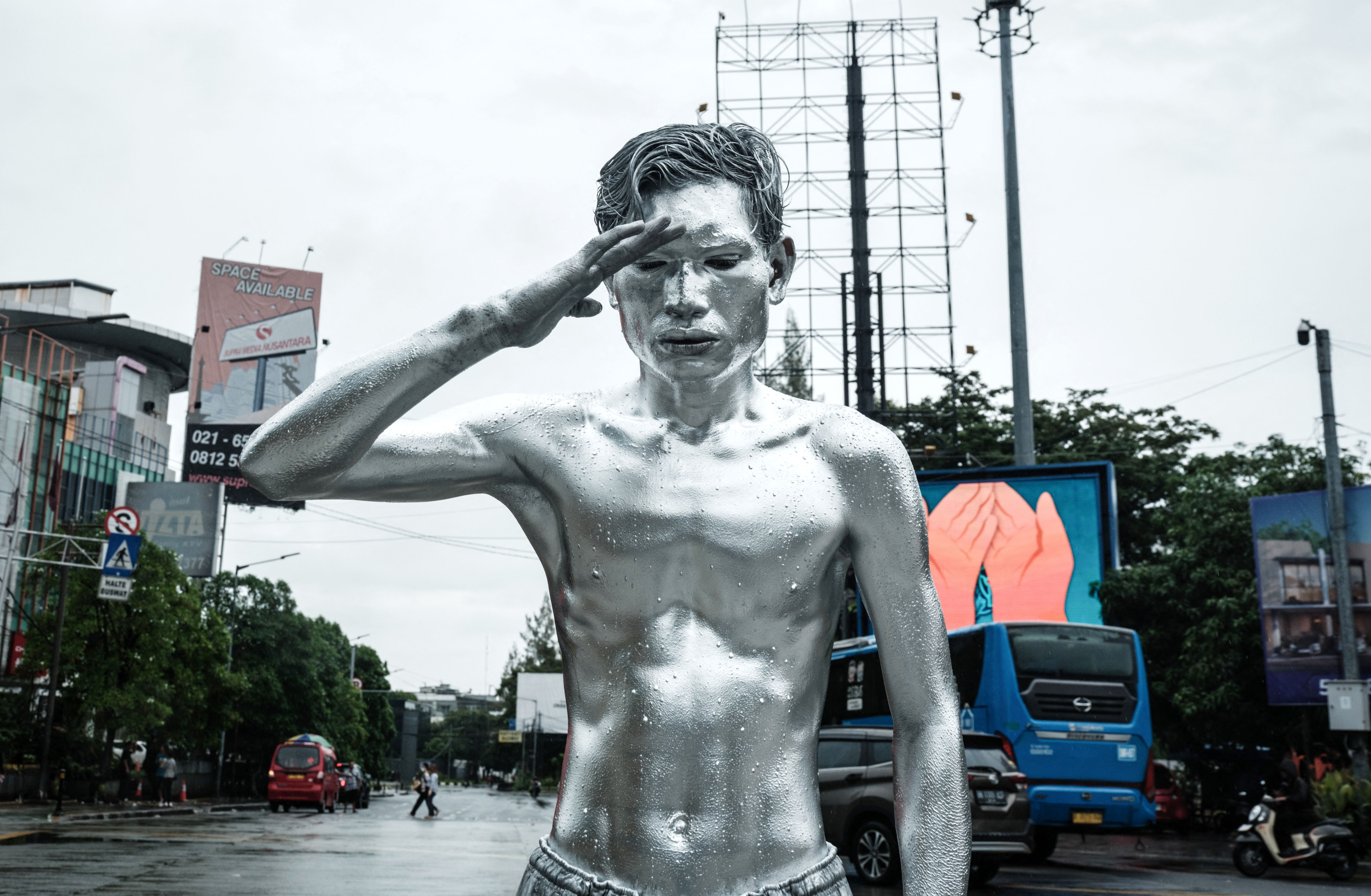 A street performer, with his body completely covered in silver paint, salutes while begging for money in a street.