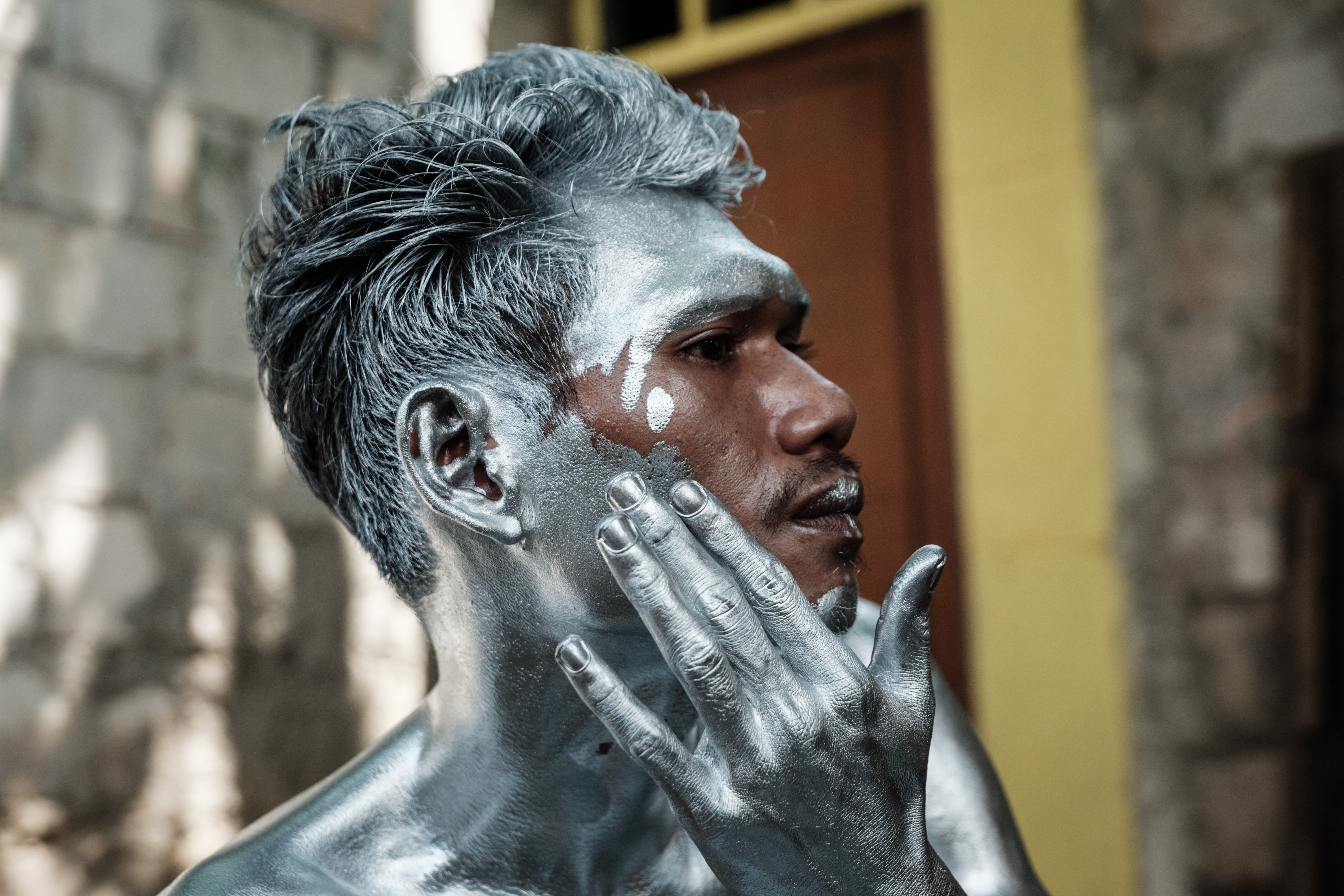 A man applies silver paint to his face and neck.