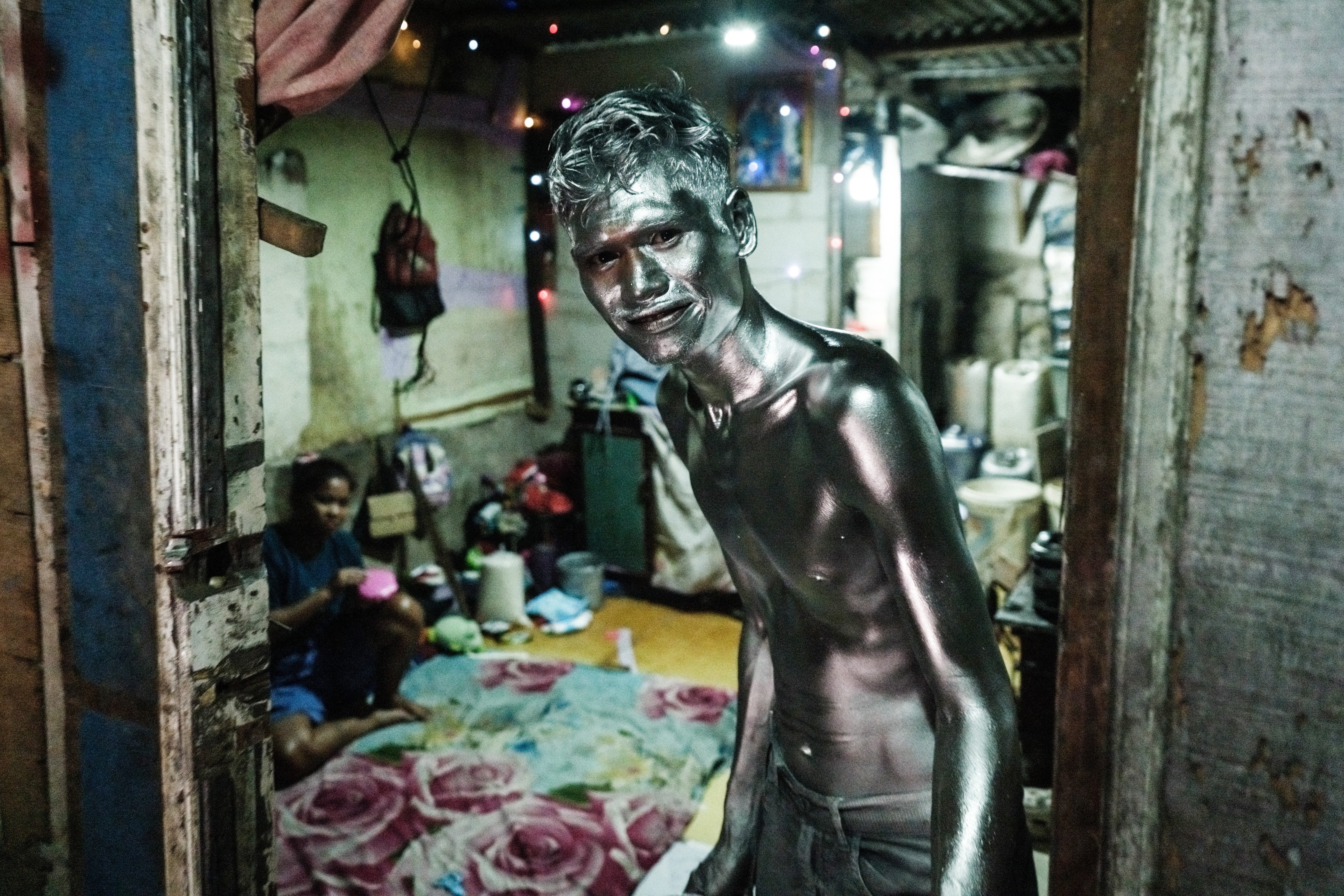 A man covered in silver paint poses while standing in the doorway of a house.