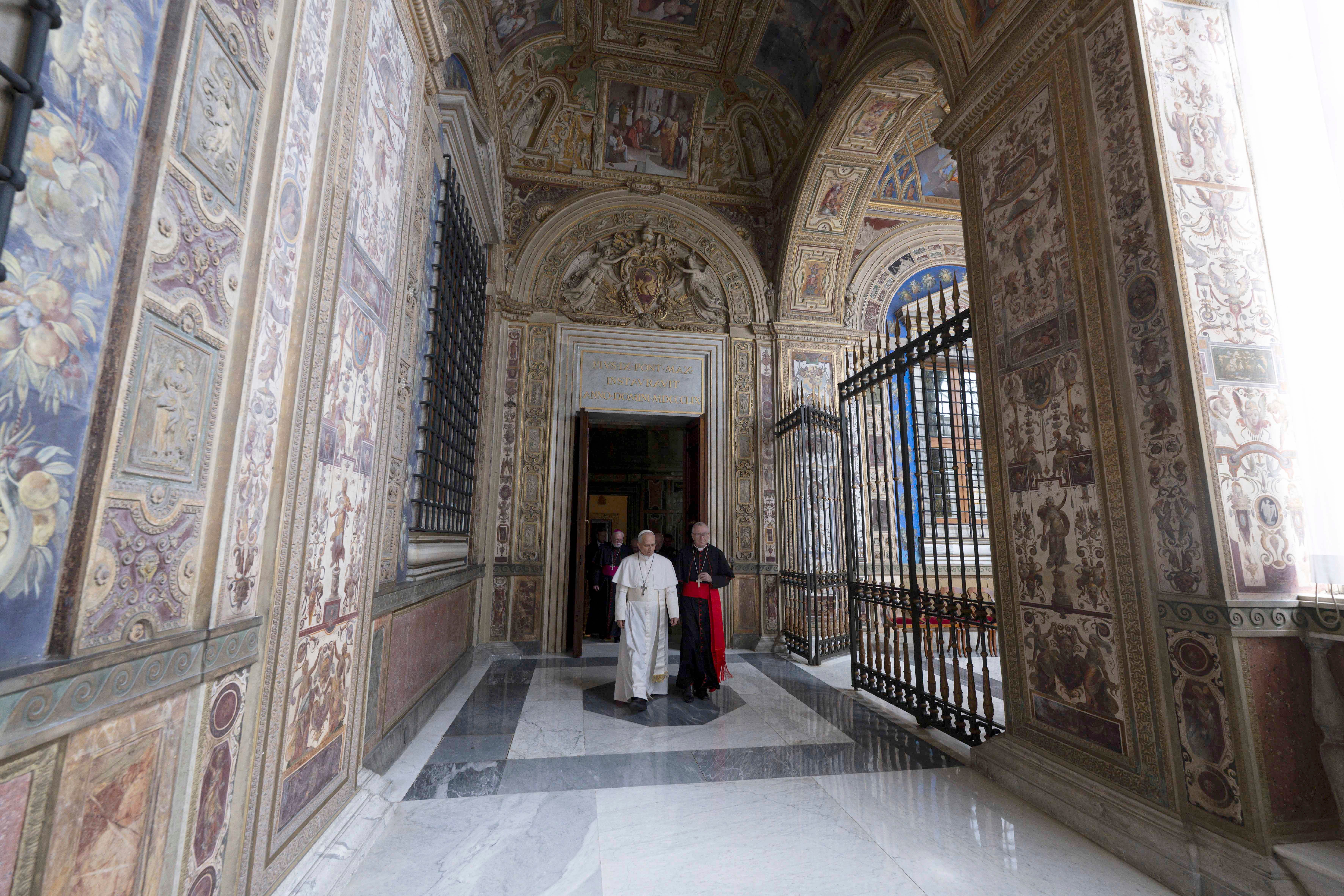 Pope Leo and two others walk through an elaborately decorated corridor