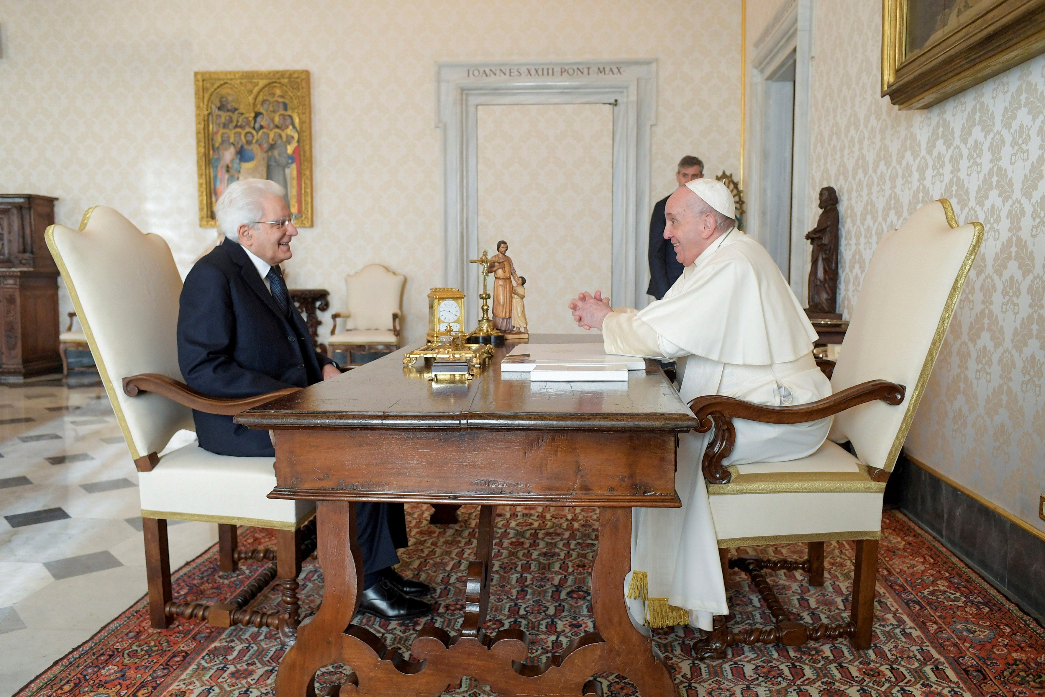 Italy's president Sergio Mattarella and Pope Francis sit across from each other at a table in a room with gold and white wallpaper