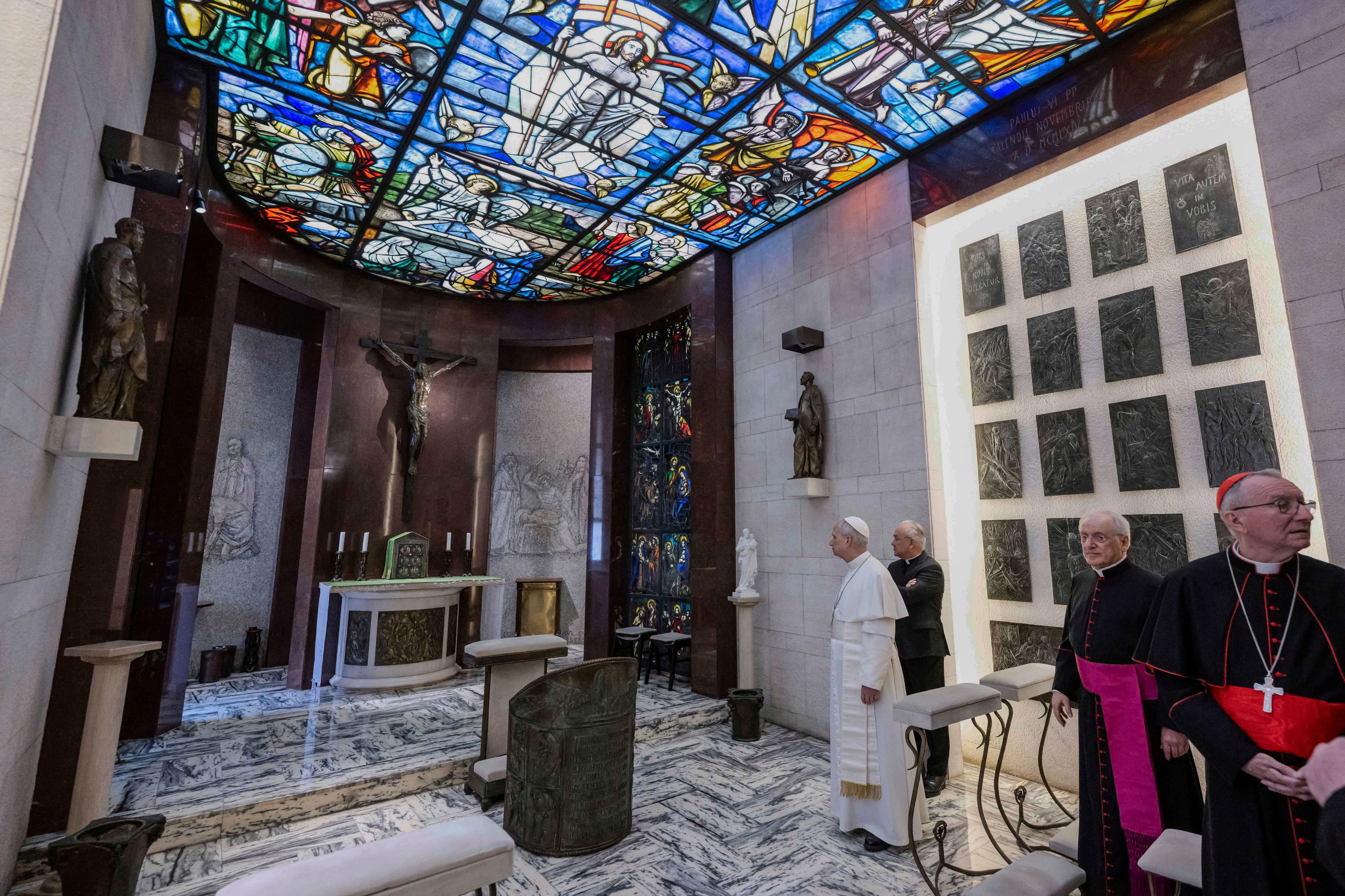 Pope Leo XIV and several men in black and red stand in a chapel with a stained glass ceiling