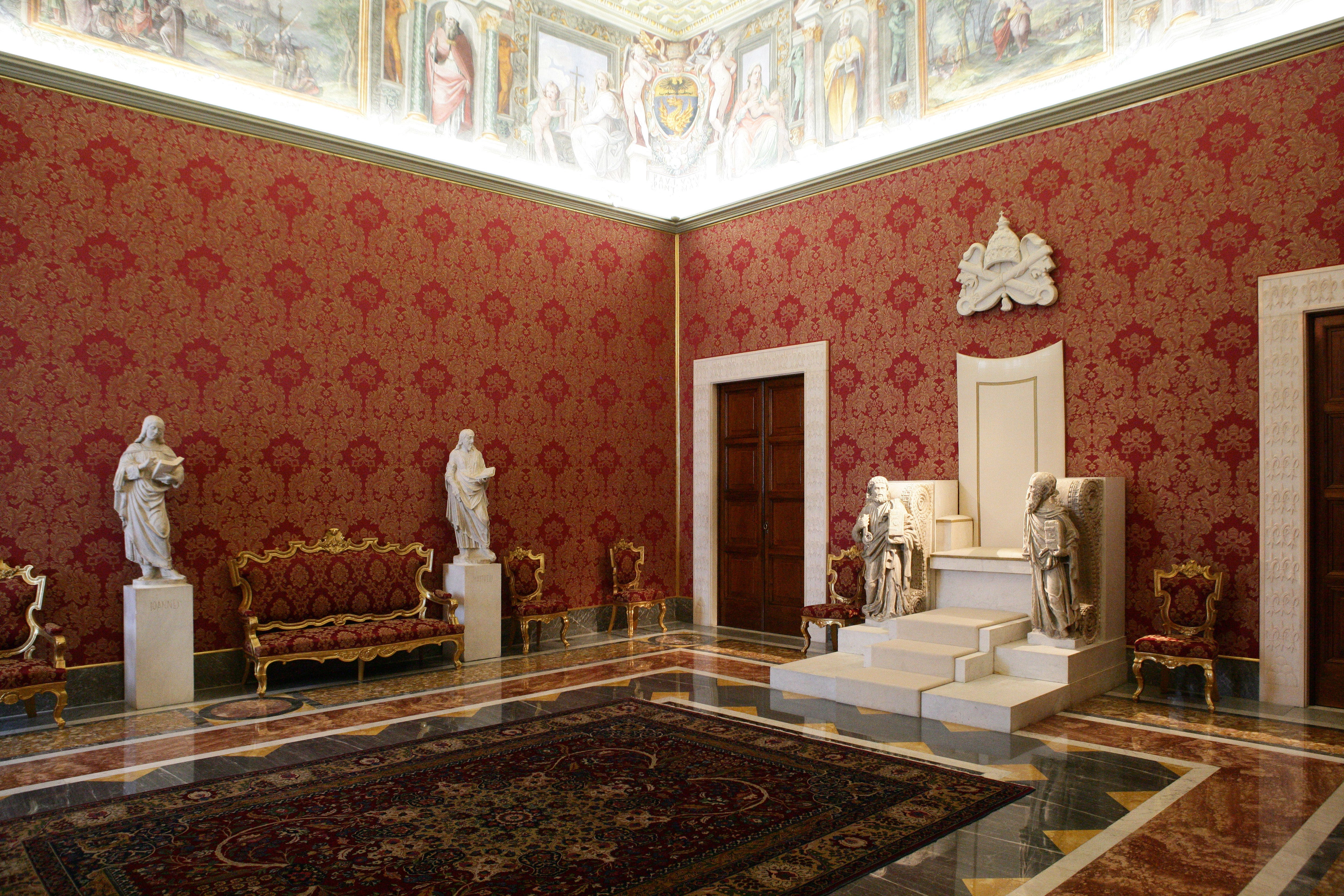 A room with red wallpaper, statues, and ornate furniture