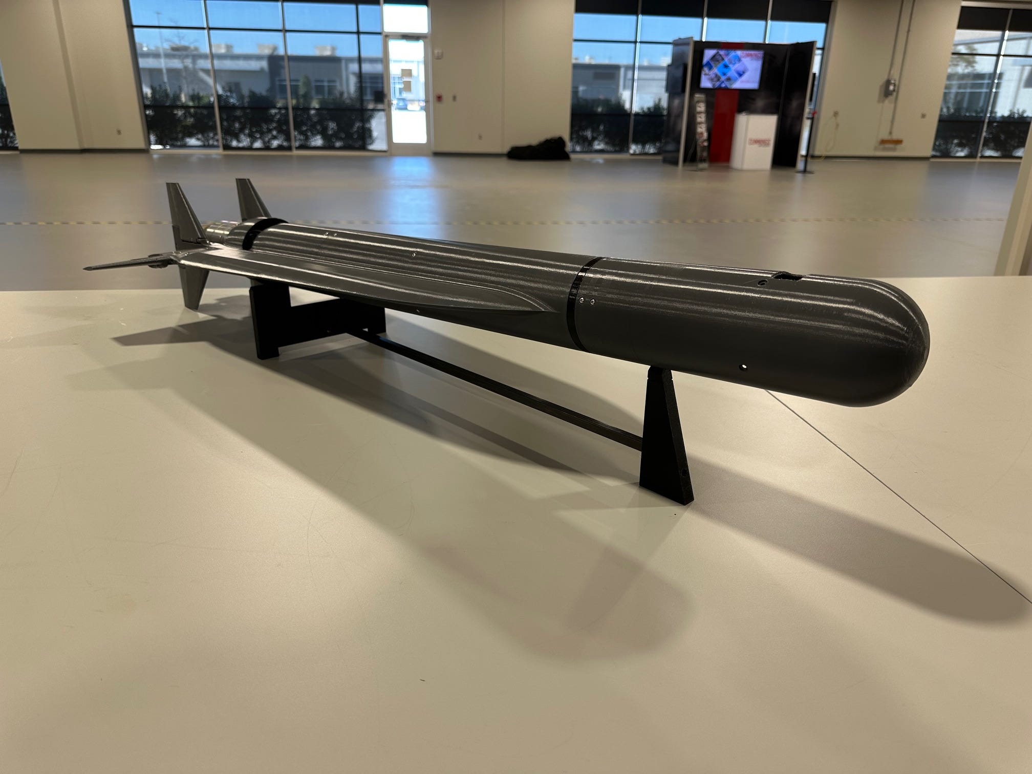 A black loitering munition sits on a white table in an office space.