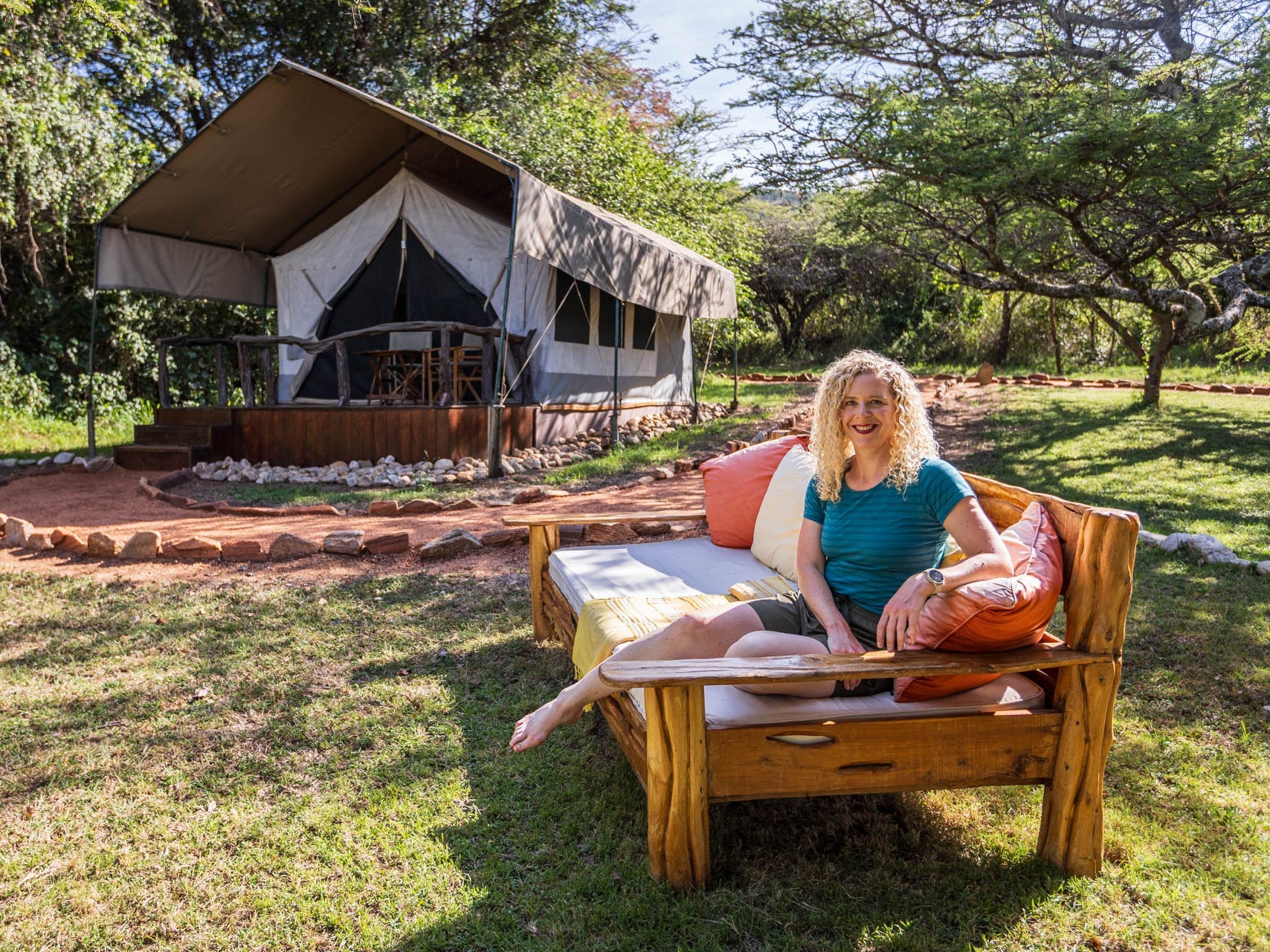 A woman is sitting on a bench outside a tent in the woods.
