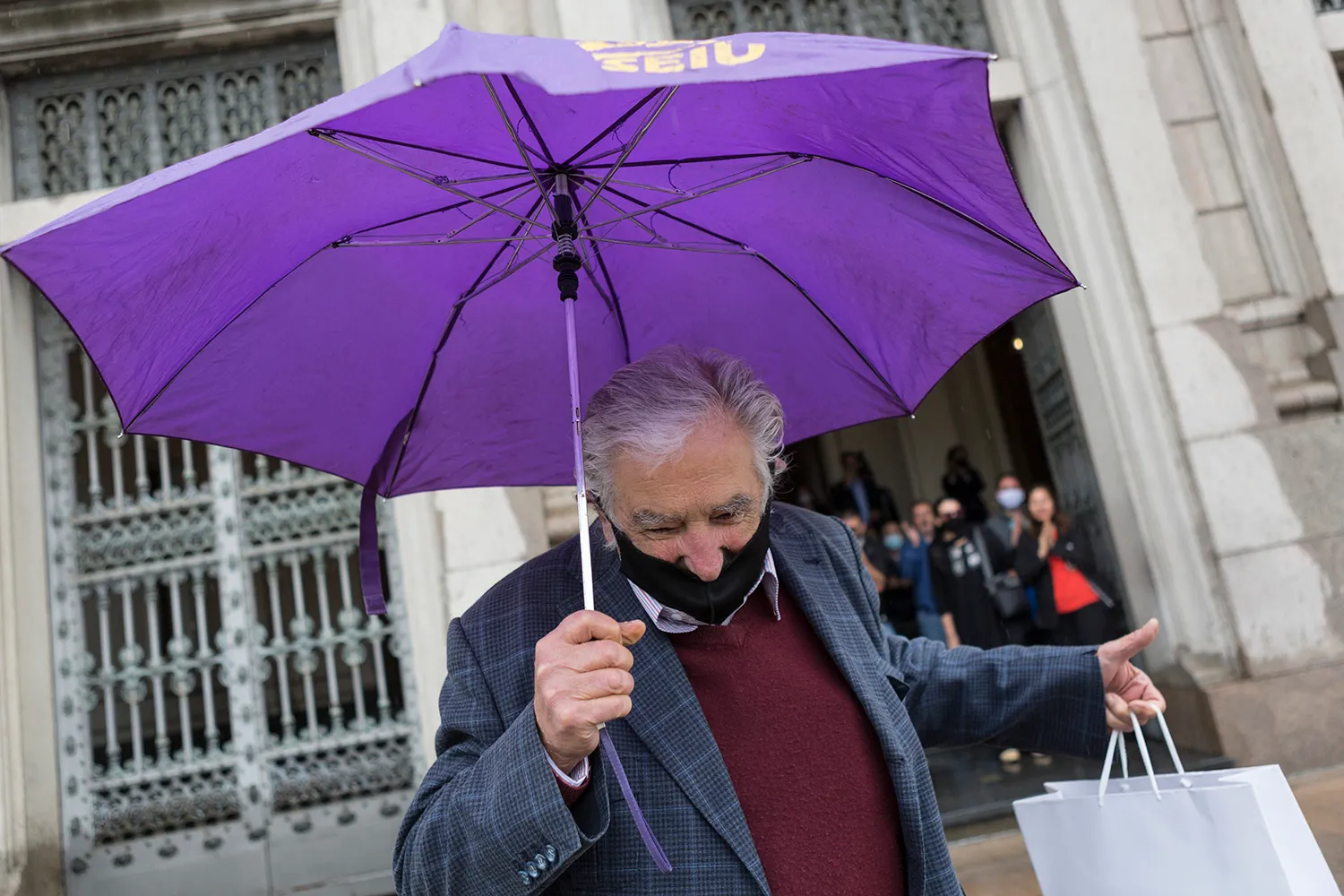 José Mujica wears a face mask and carries an umbrella.