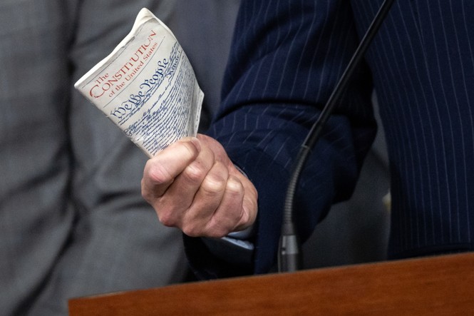 A person holds up a small copy of the Constitution of the United States