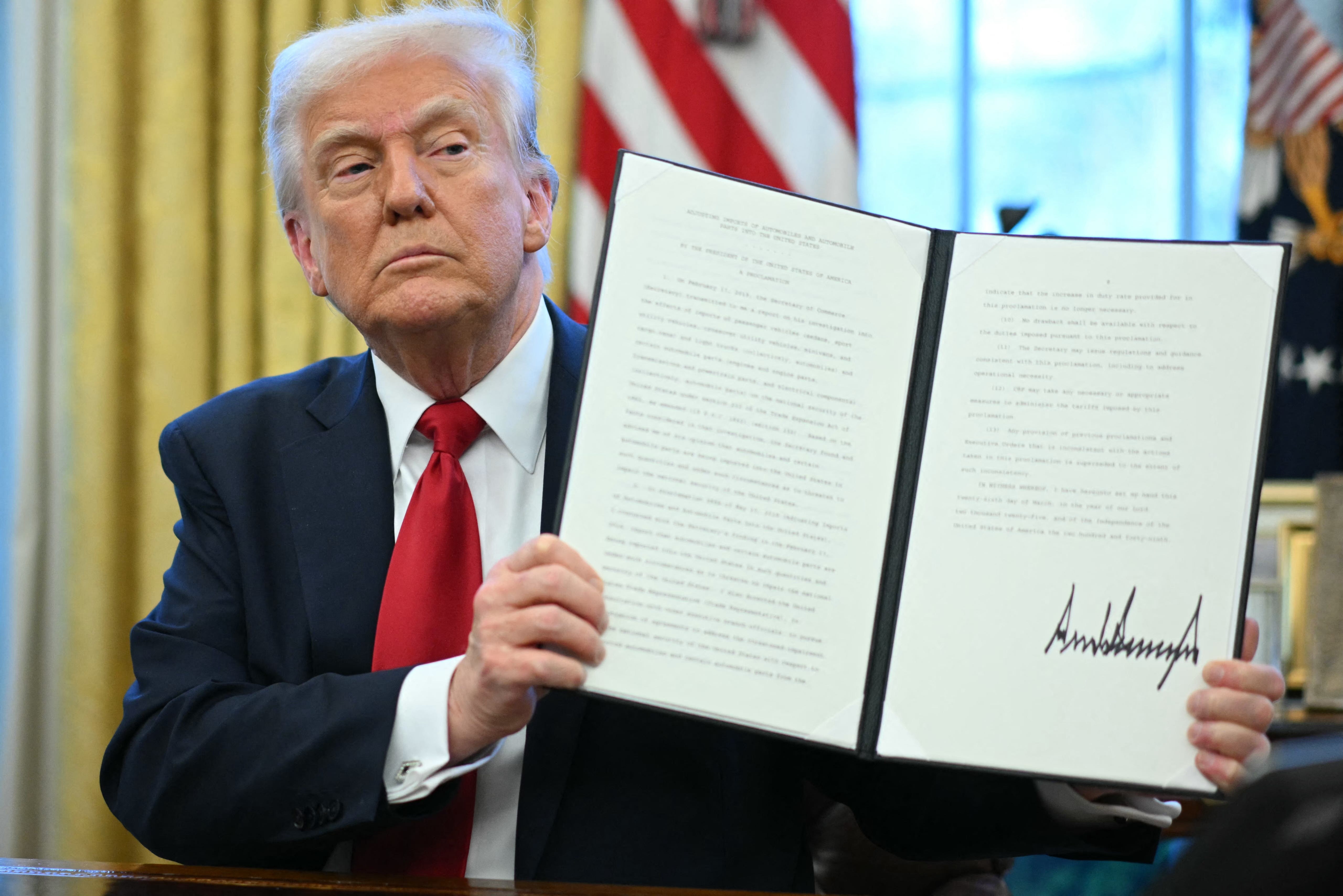 US President Donald Trump displays an executive order he signed announcing tariffs on auto imports in the Oval Office of the White House in Washington, DC, on March 26, 2025.
