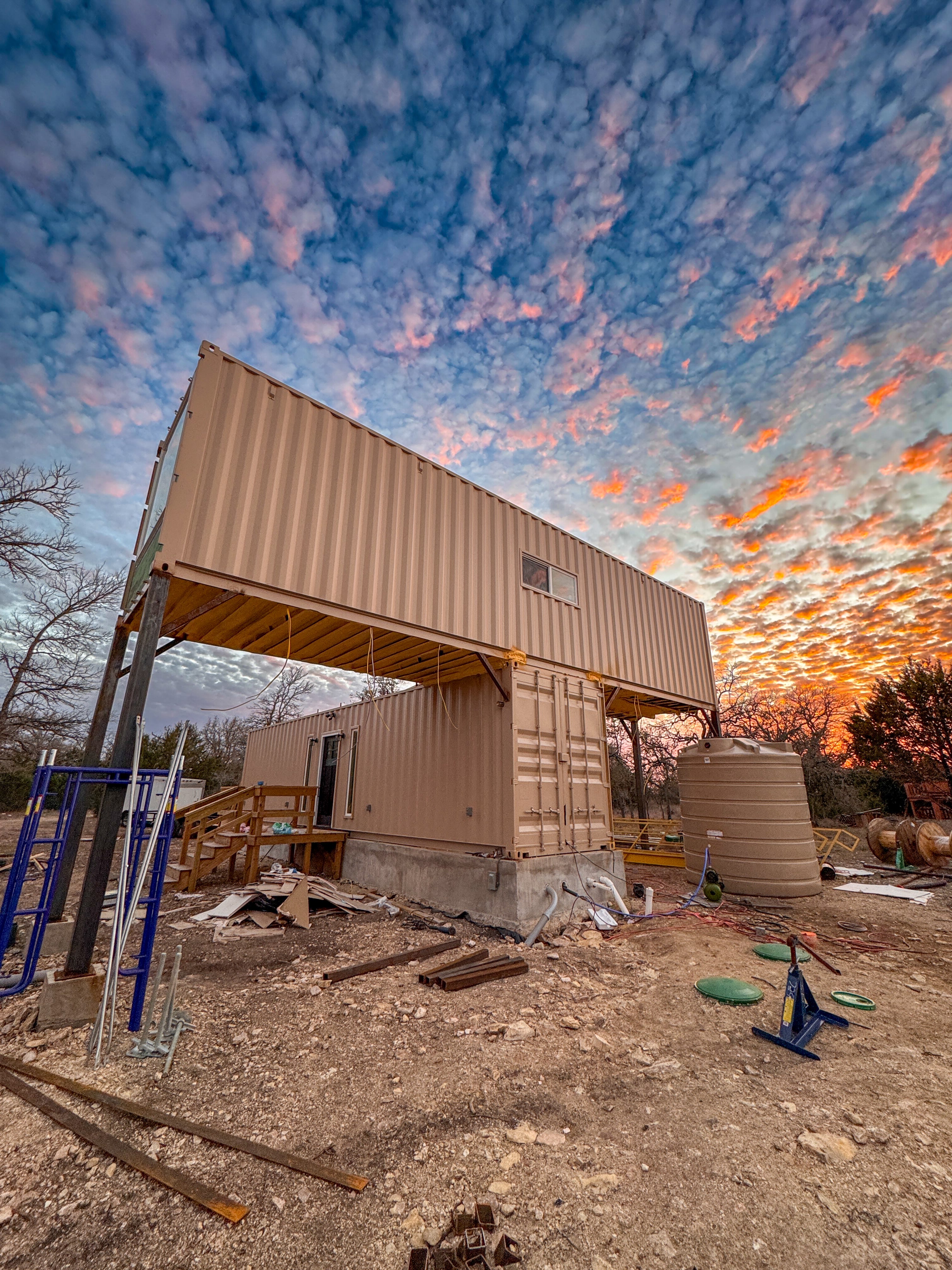 A shipping container home at sunset. A water tank sits next to the home.