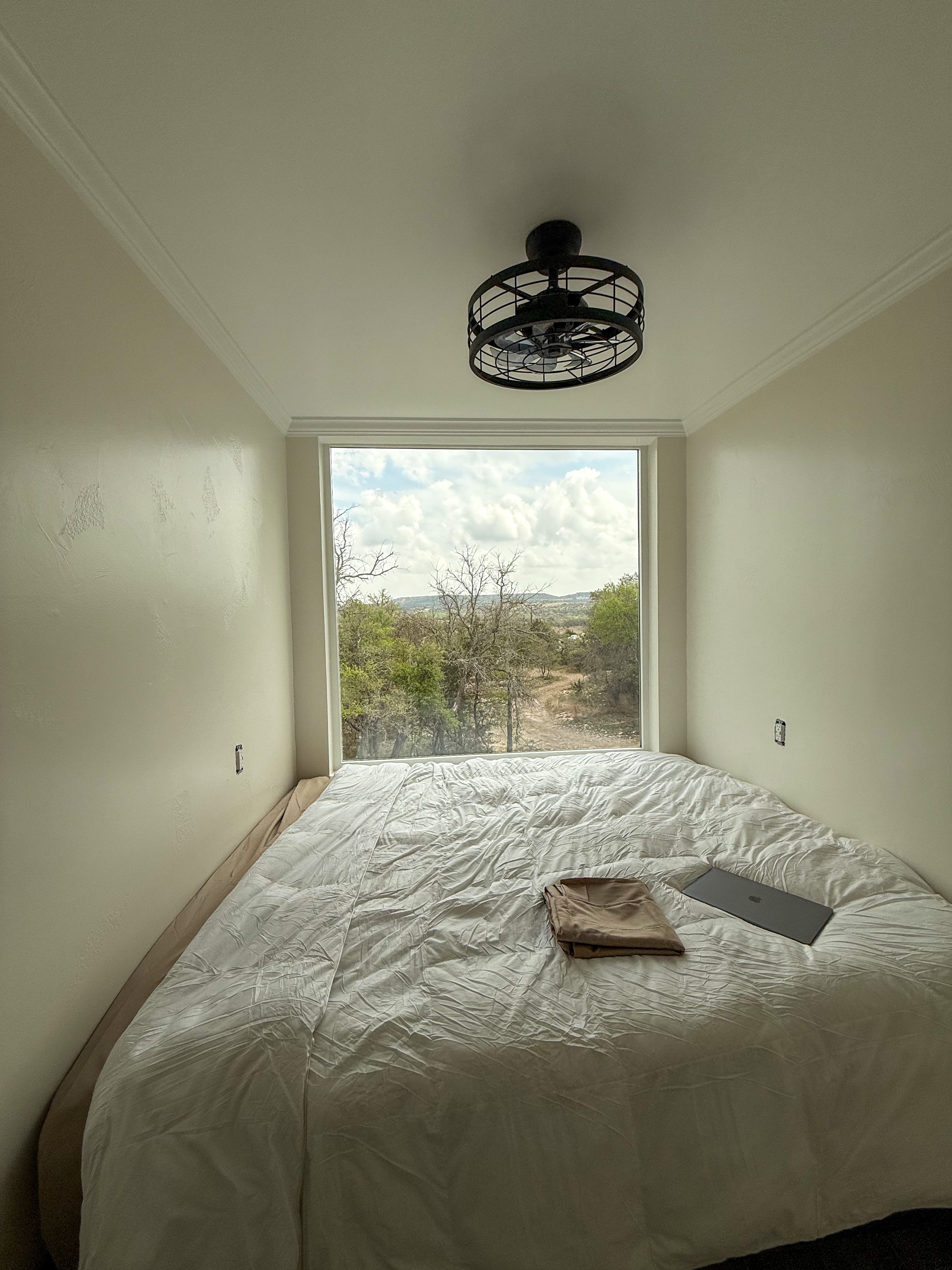 A bedroom in a tiny home. A large window covers a back wall.
