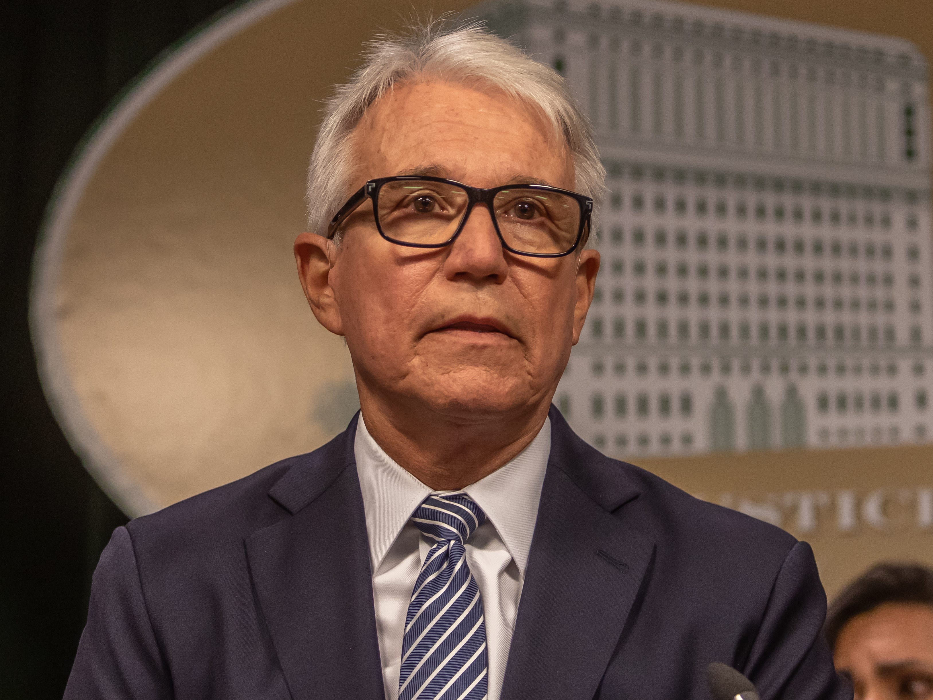 An image of a man wearing a blue suit, blue and white striped ties, and glasses.