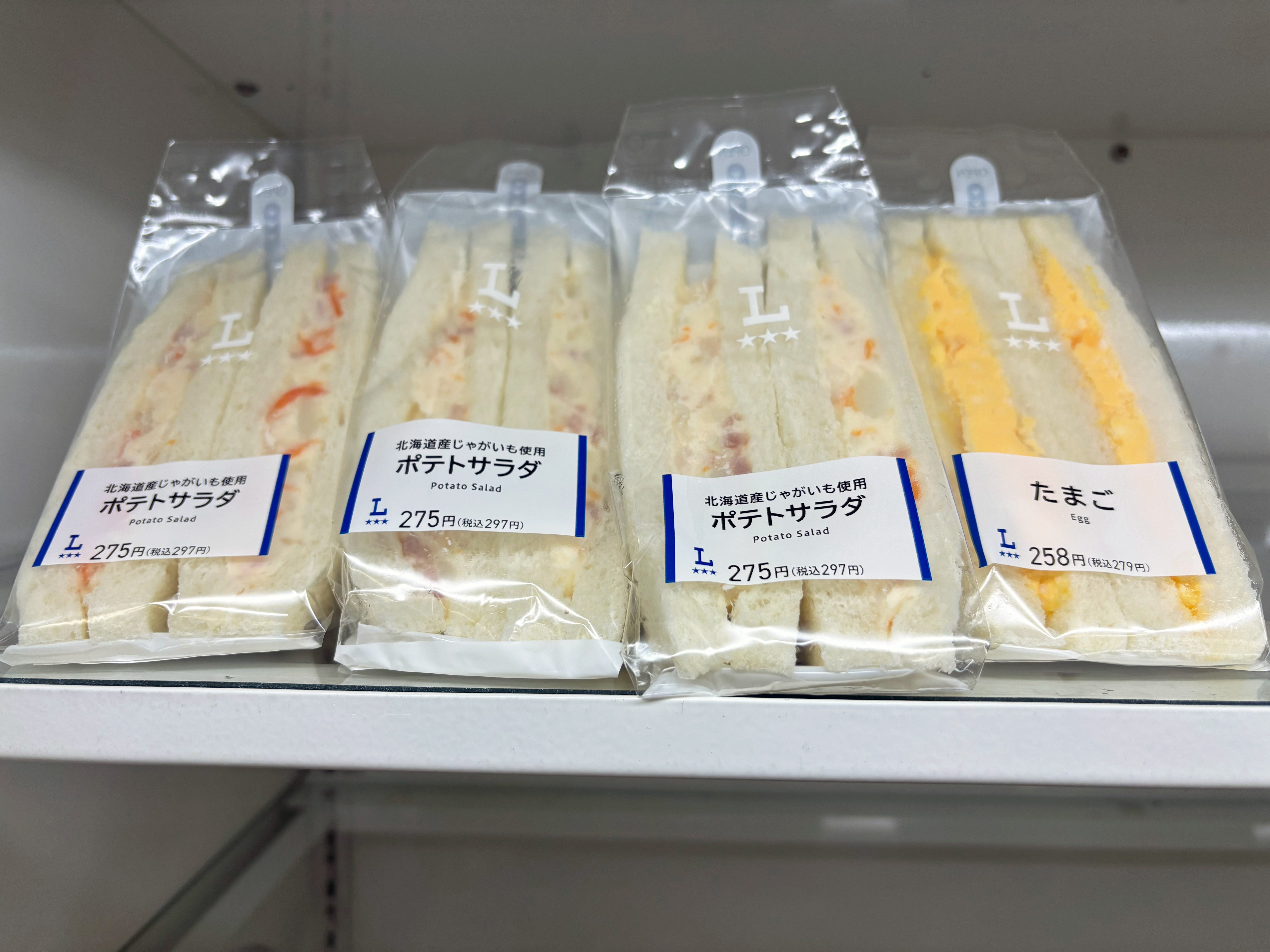 Four sandwiches wrapped in plastic on a white shelf