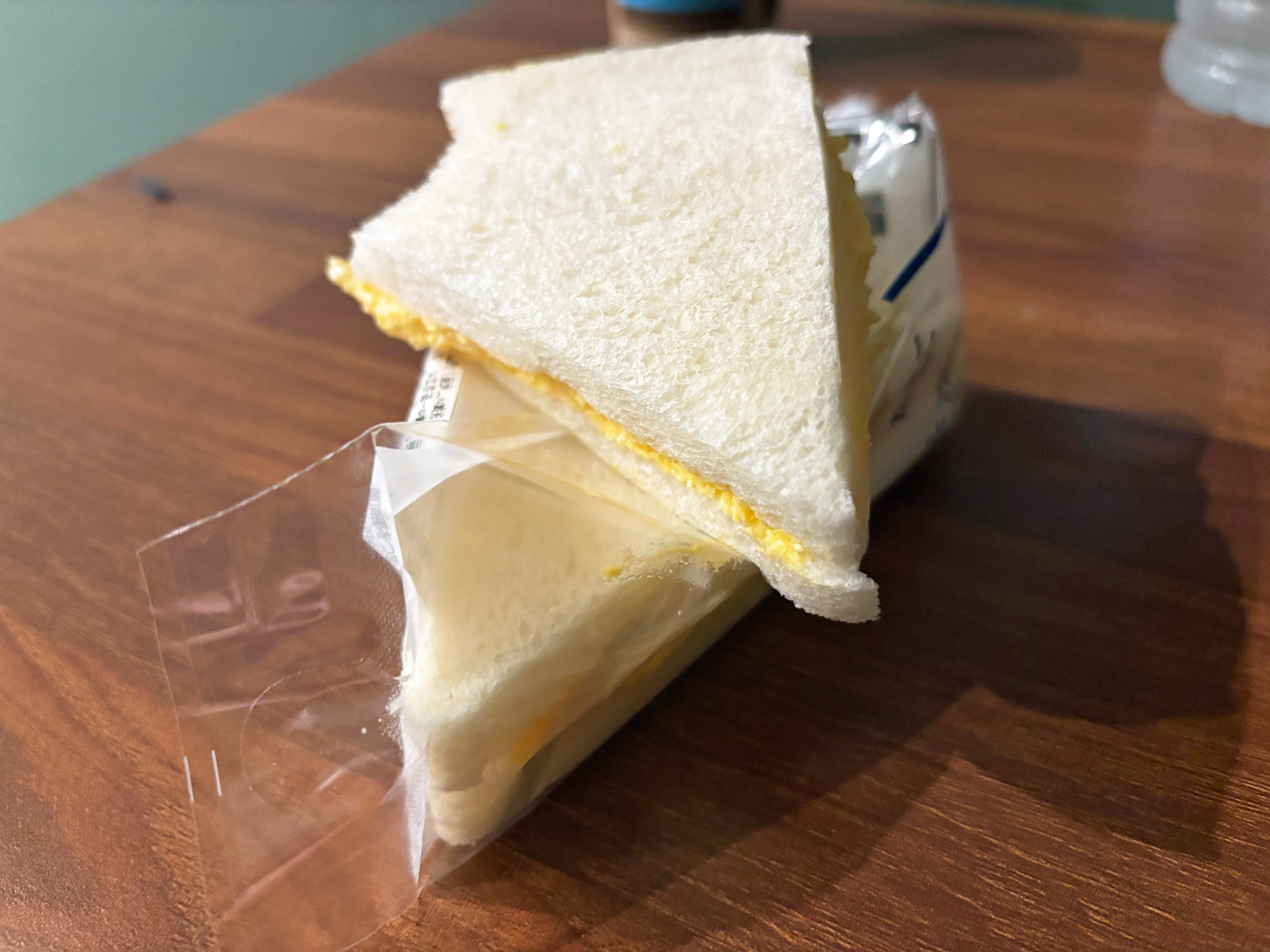 An egg sandwich with half on top with a bite missing on a wooden desk