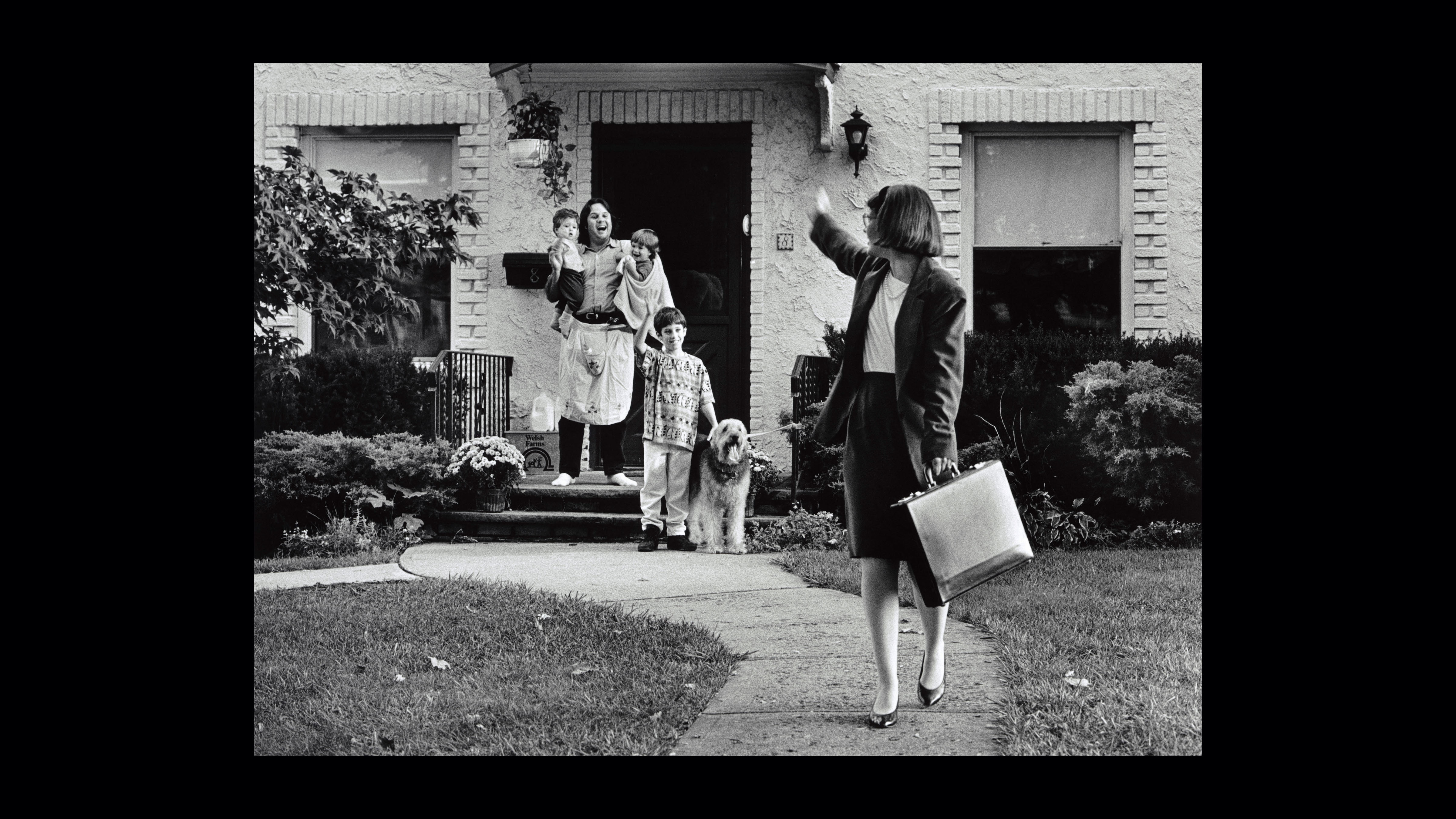 Photo of a mother leaving for work, waving goodbye to her husband and children