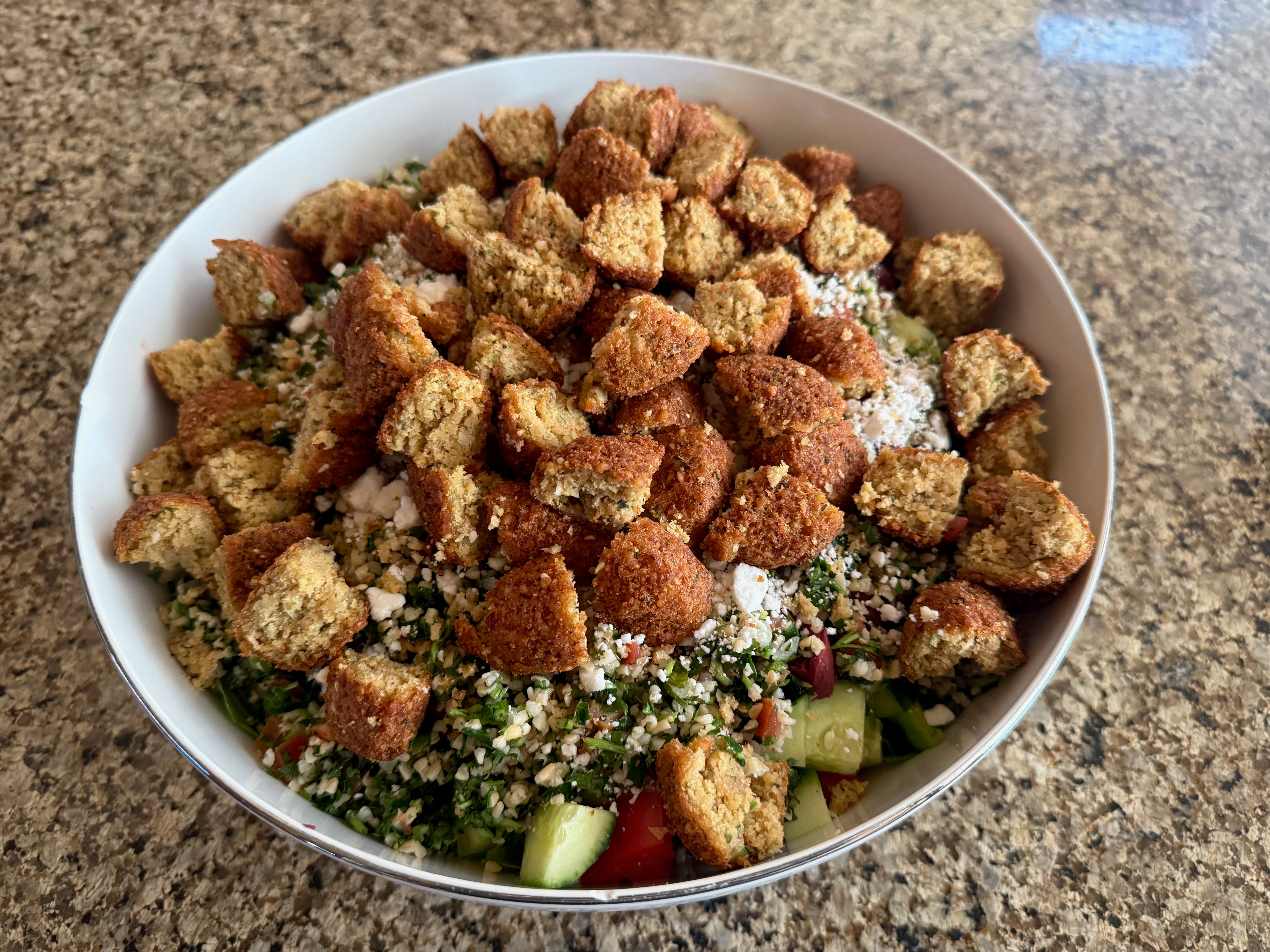 A salad with romaine lettuce, tomatoes, cucumber, Tabbouleh, and falafel.