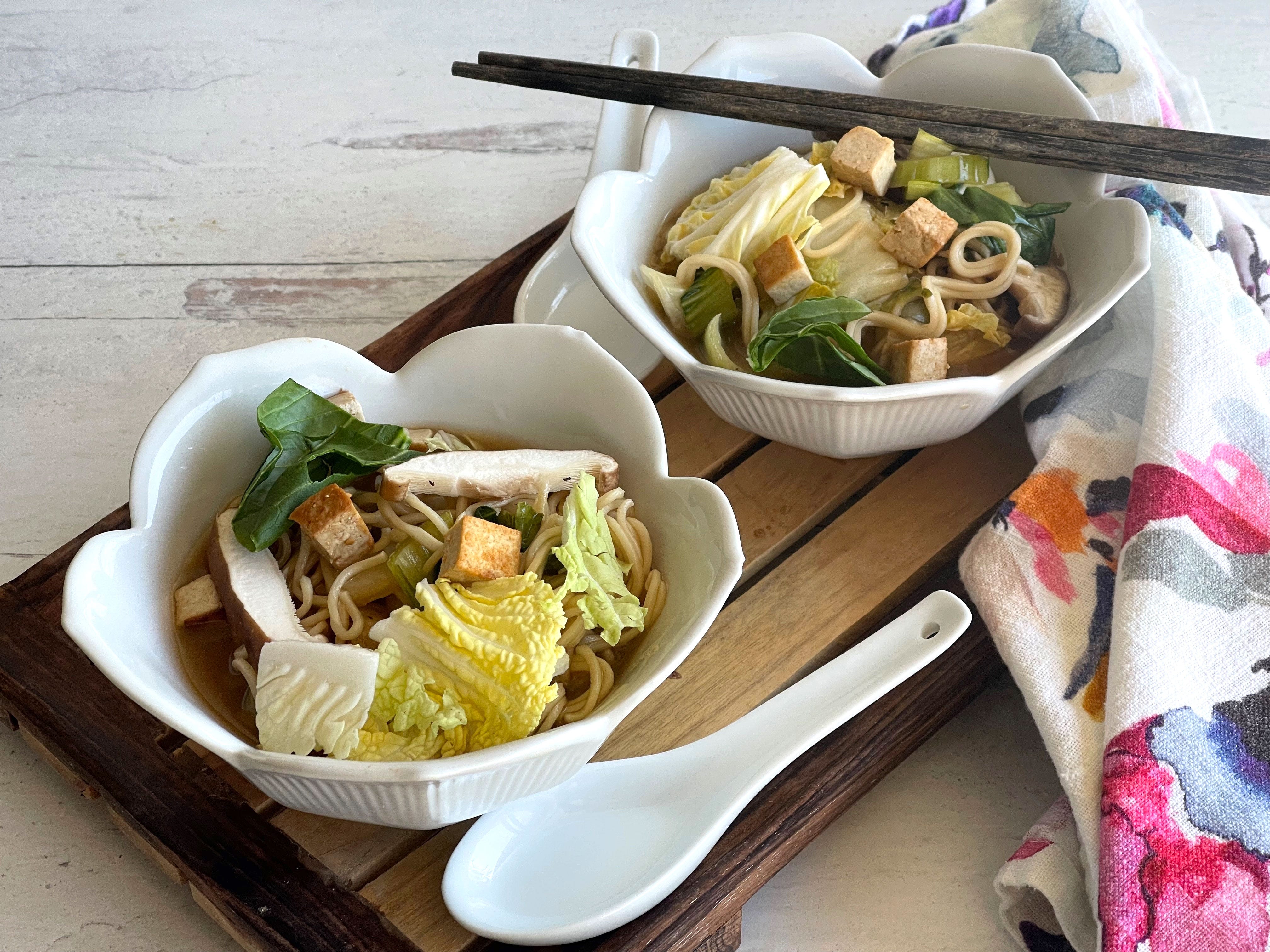Two bowls of ramen with a pair of chopsticks and a white spoon.
