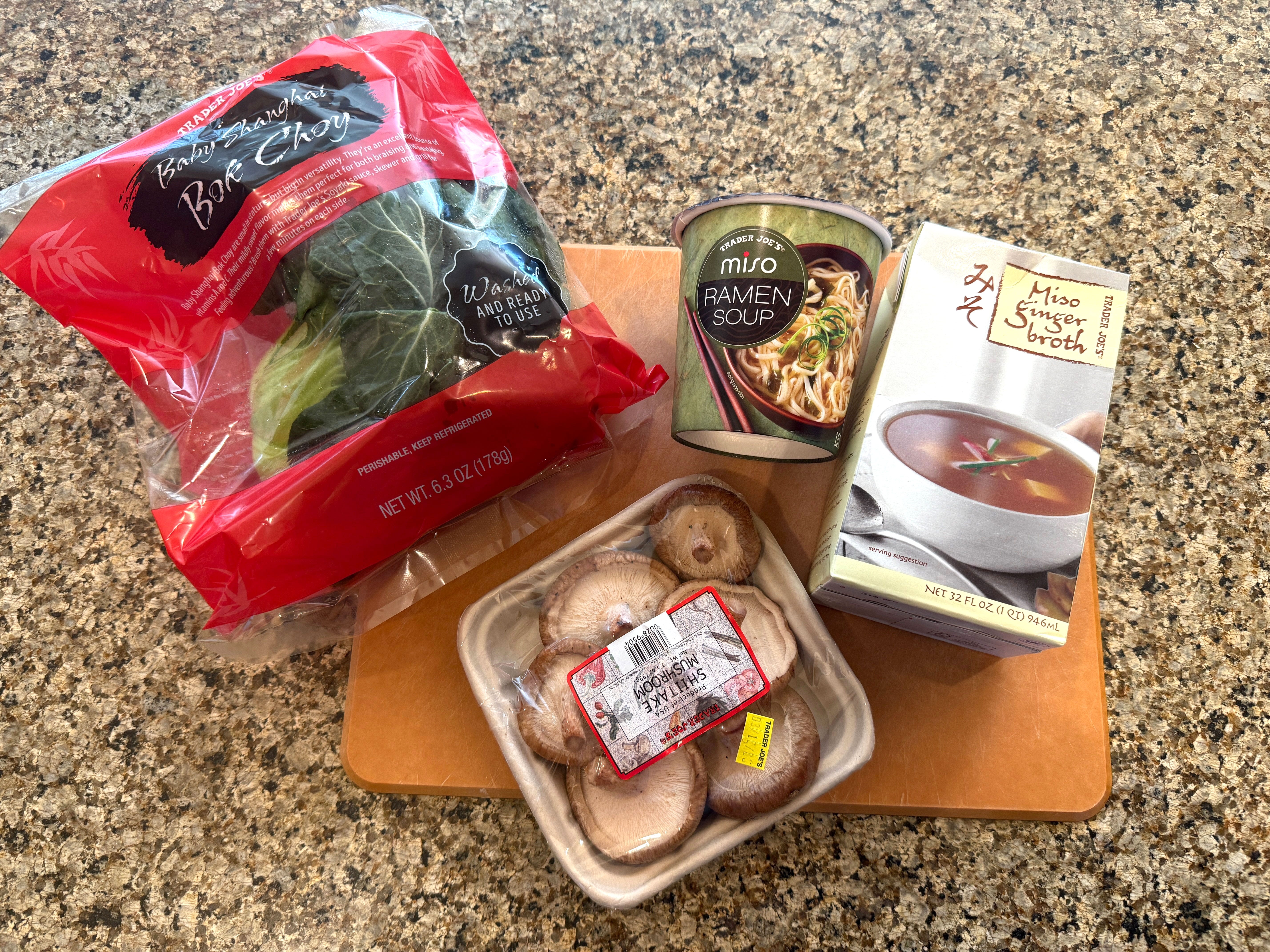 A bag of bok choy, a container of shiitake mushrooms, a container of Trader Joe's miso ramen soup, and a box of Trader Joe's miso ginger broth.
