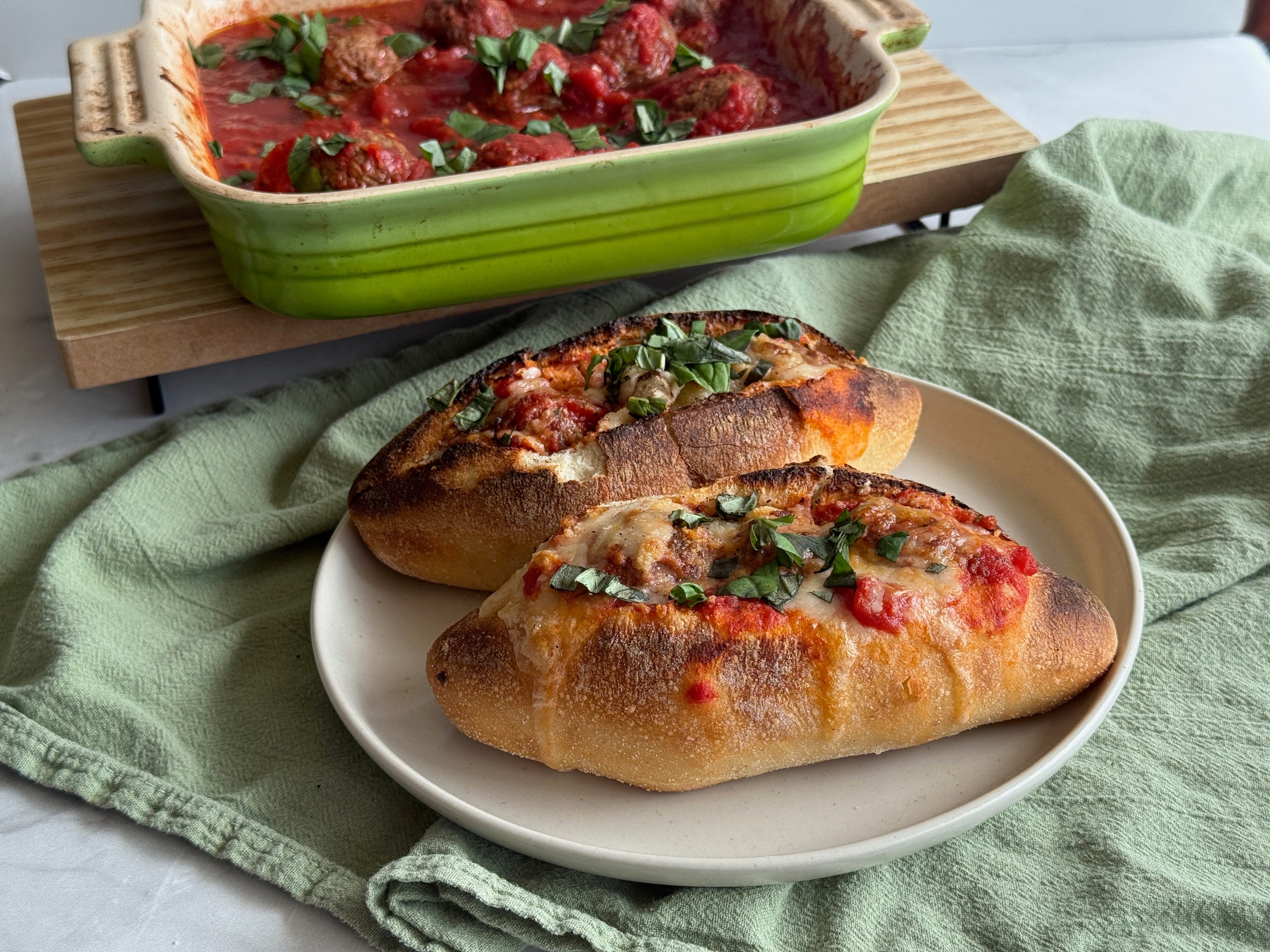 A casserole of meatballs and two meatball sandwiches on display.