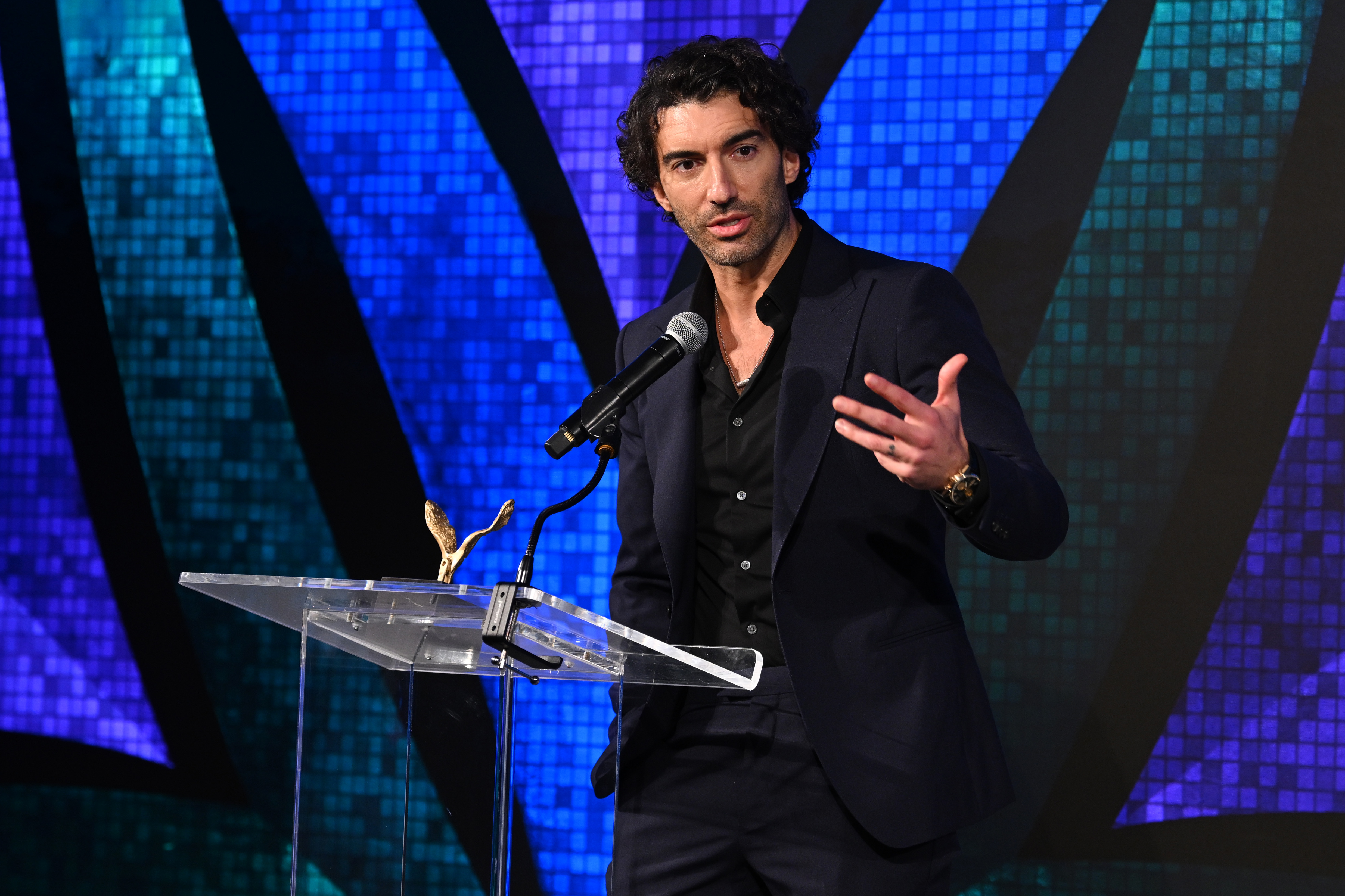 Justin Baldoni speaking at a podium. 
