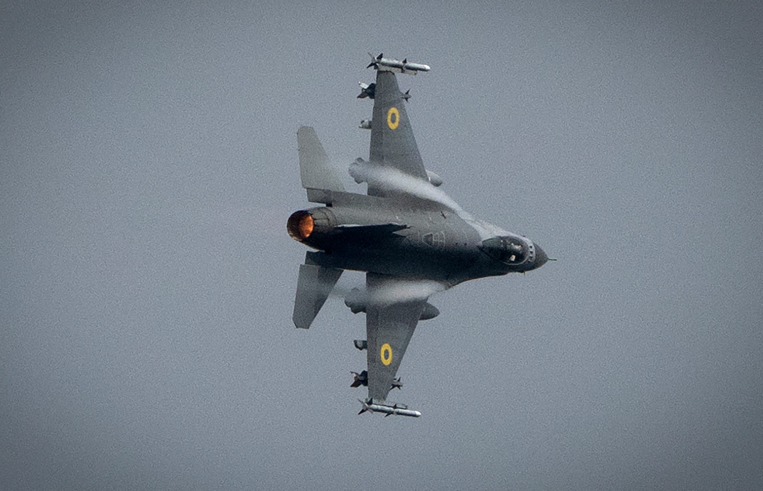 An F-16 fighter jet flying across gray skies.