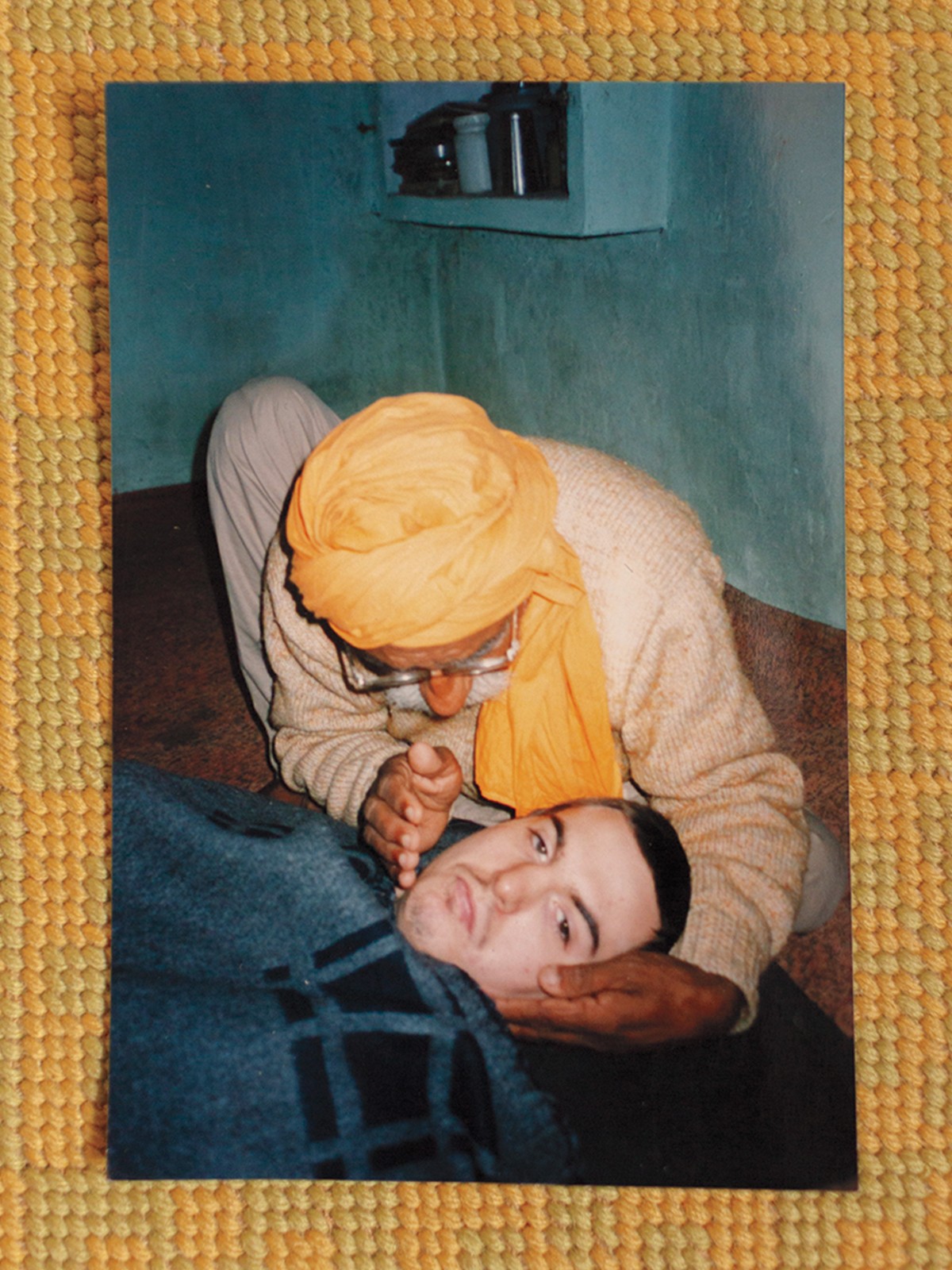 photo of person with yellow scarf wrapped around head, cradling the head of young man lying under blanket