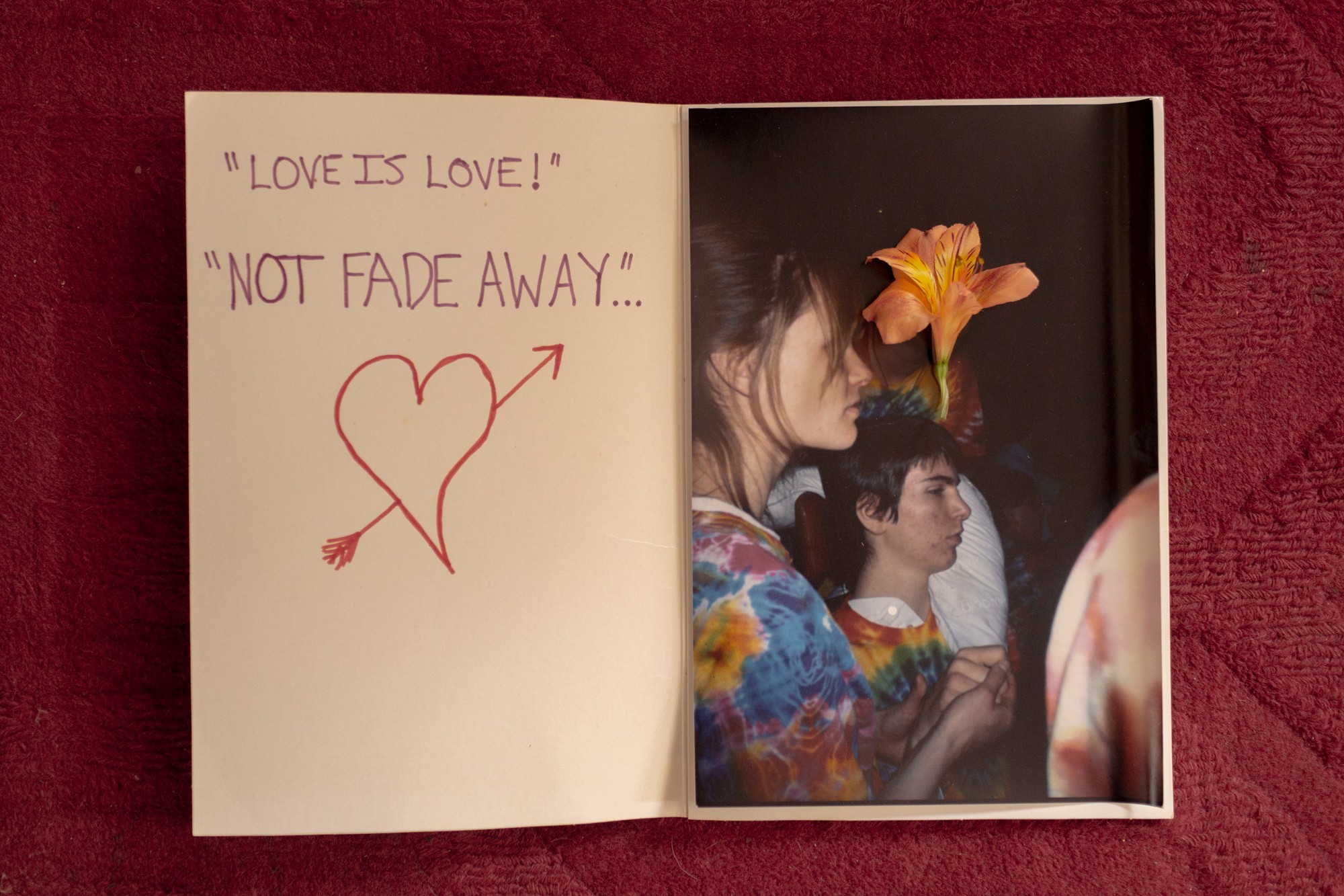 photo of hand-written card with words 'LOVE IS LOVE' AND 'NOT FADE AWAY' alongside heart with arrow on left page and photo of people with flower on right 