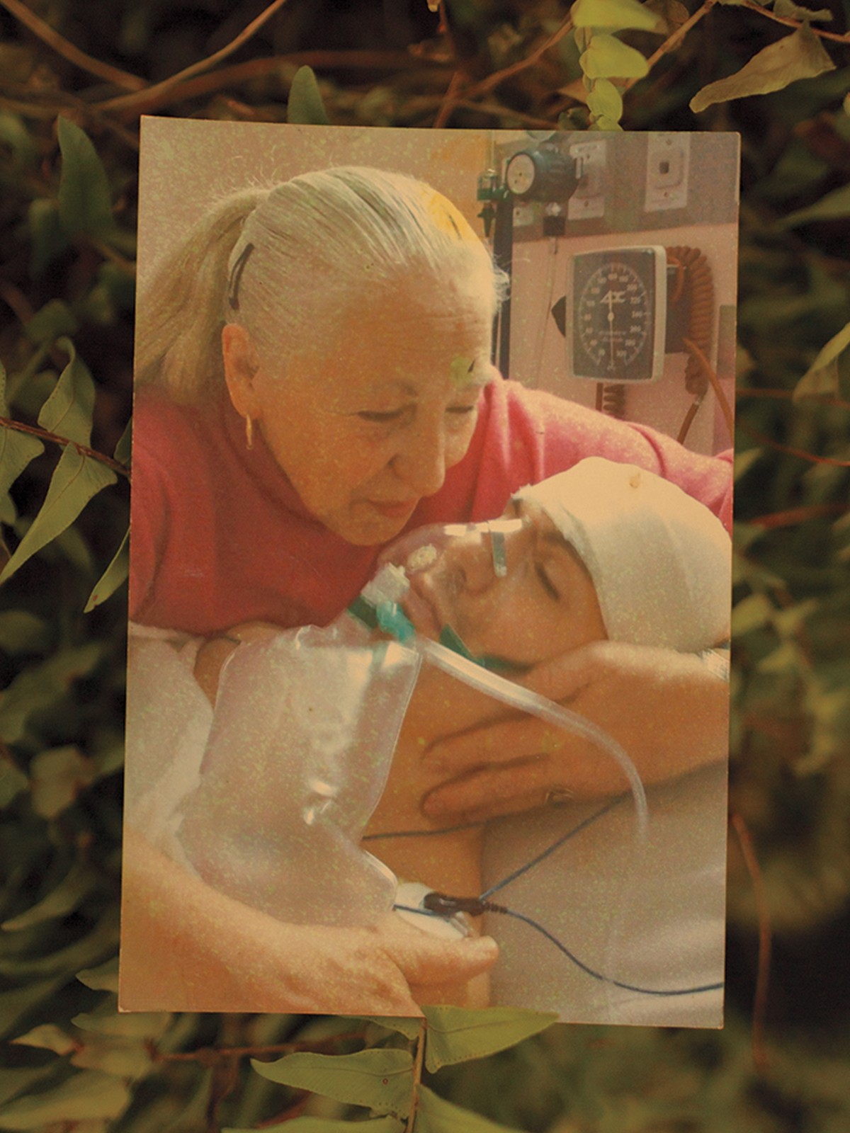photo of white-haired woman in ponytail cradling bandaged head of man with breathing mask and monitors in her arms