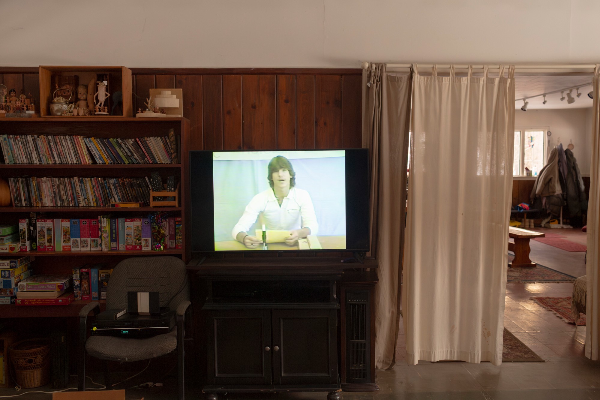 photo of living room with shelves and a TV displaying video of young man at desk giving presentation