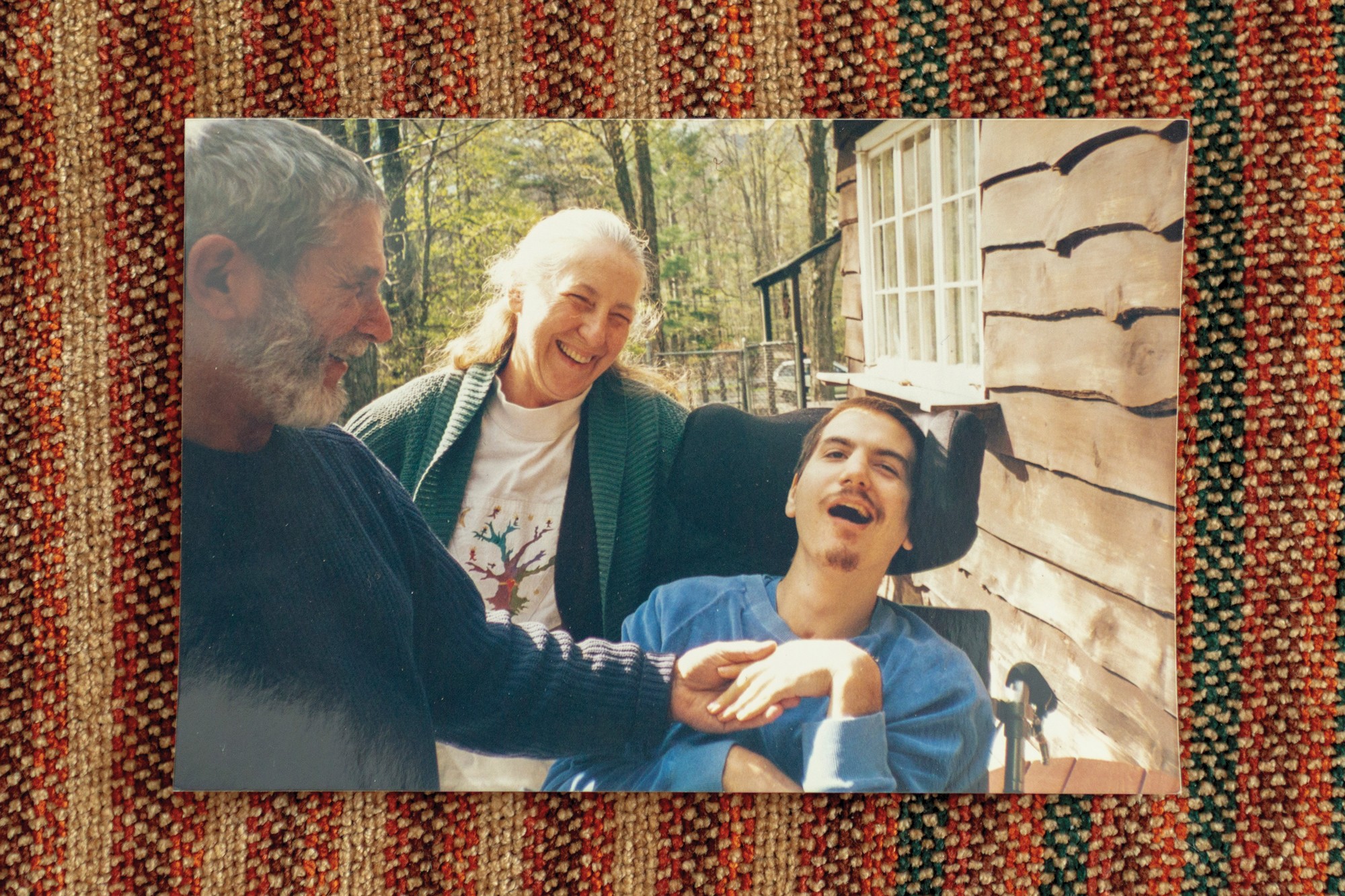 photo of man smiling and woman laughing, standing next to motorized chair with young man with mustache, eyes and mouth open.