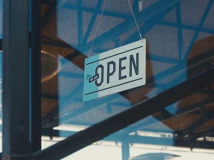 An "Open" sign on a window with black metal beams in the background