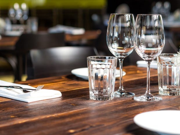 A wooden table with neatly arranged silverware and empty water and wine glasses