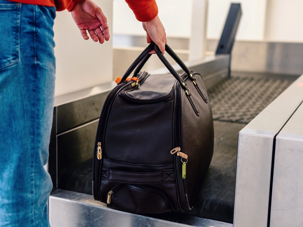 A person wearing blue jeans and a red shirt puts a black bag on a scale at an airport