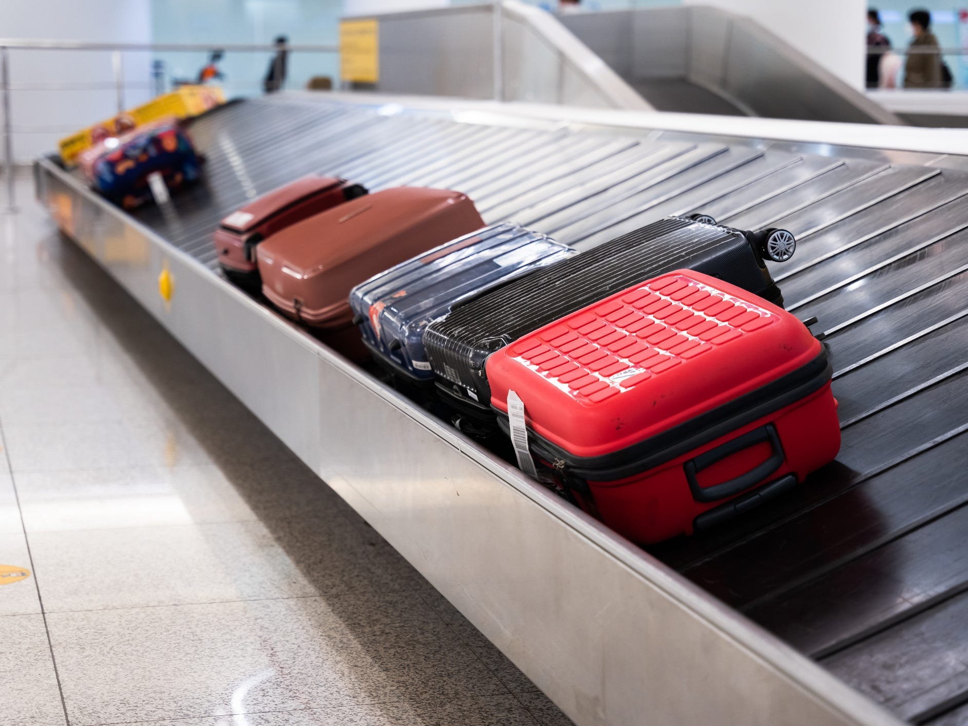 Several suitcases, including red, black, and blue bags, on a conveyor belt at airport