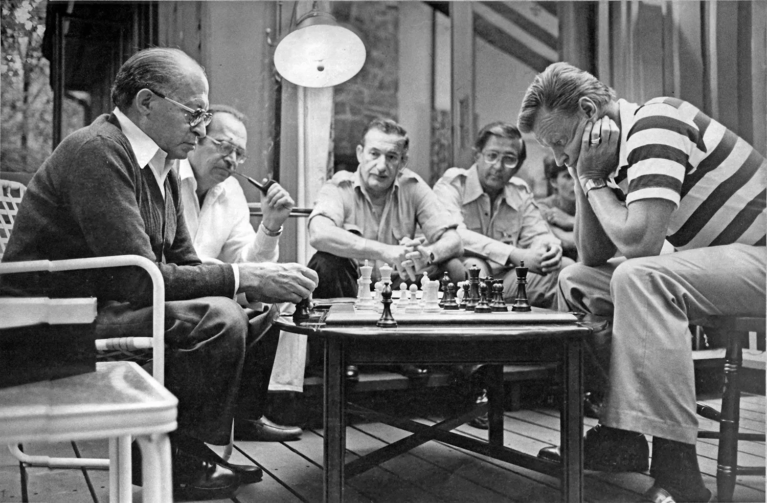 Several men sit around a chess board on a table in a room at Camp David