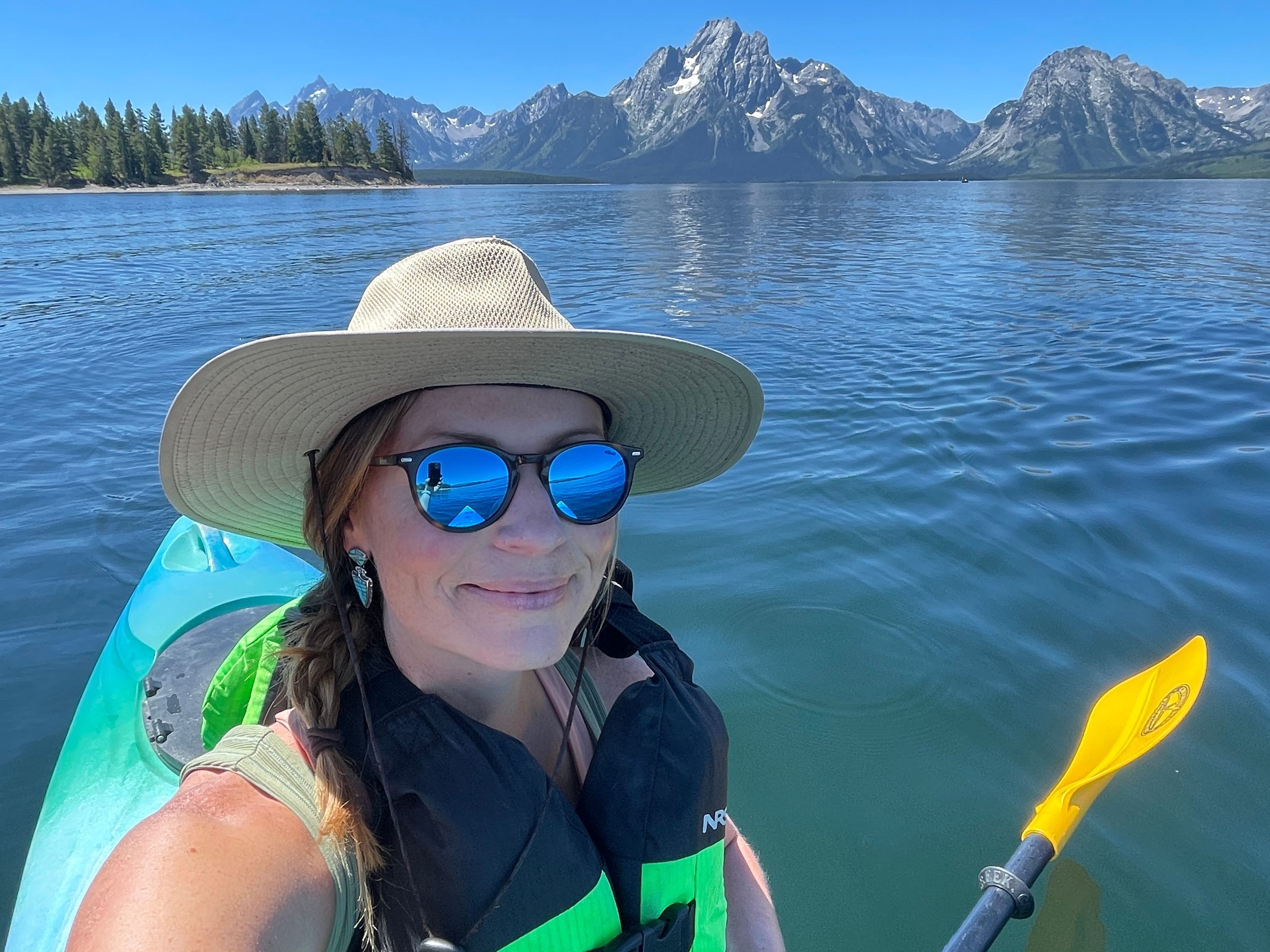 A woman sitting in a canoe with a life vest on, with mountains and trees behind her.