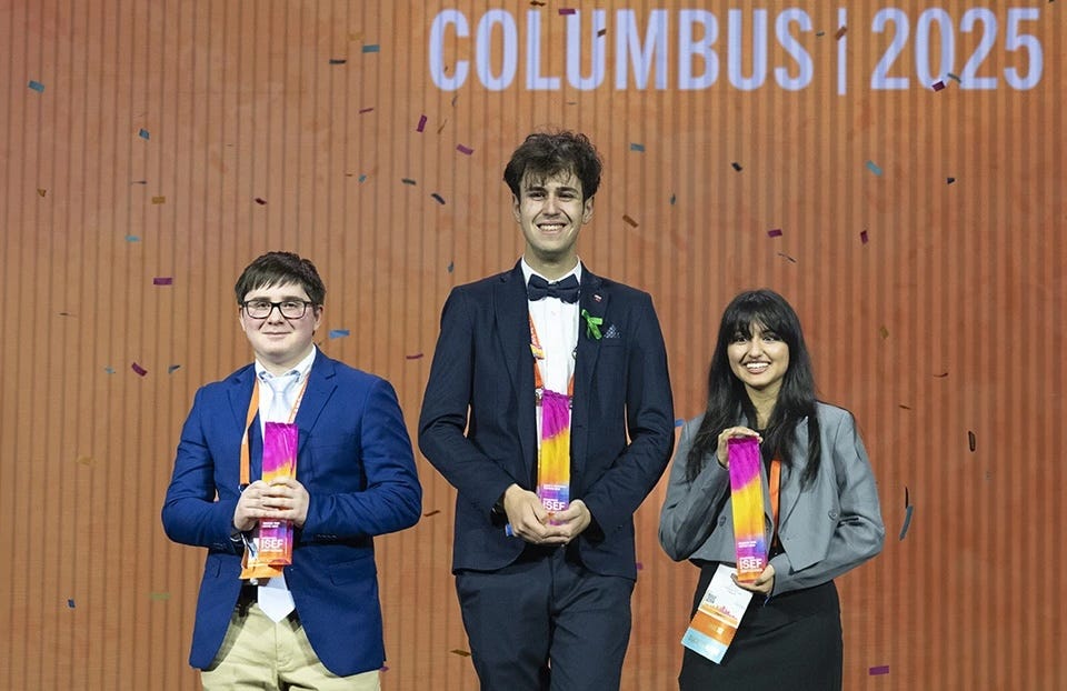 three young people in business attire smiling holding pink and gold awards on a stage