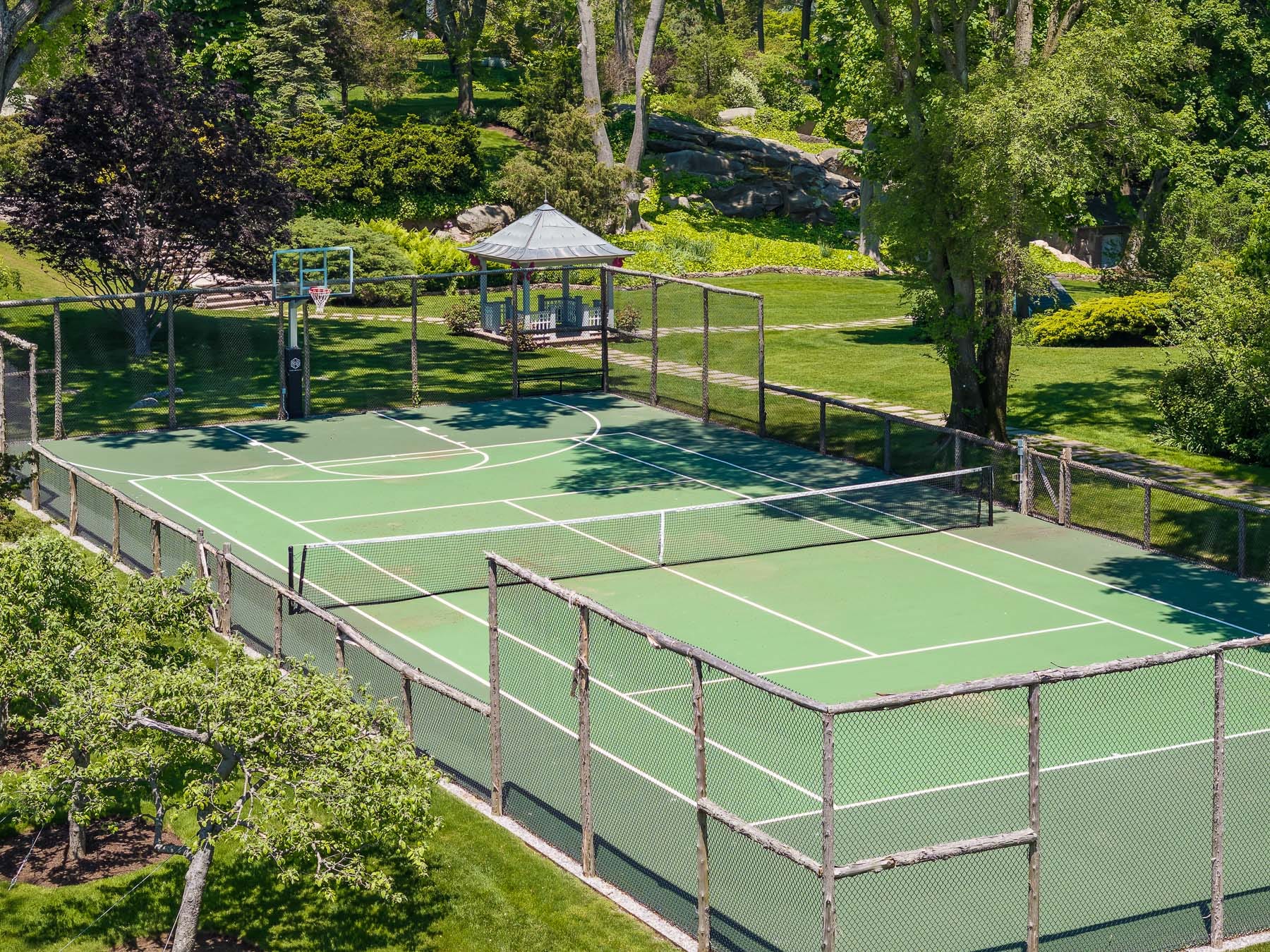 A combined tennis and basketball surrounded by trees.