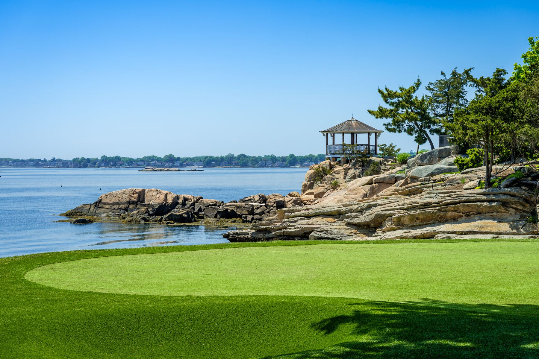 A putting green overlooking the water, with a gazebo atop some rocks in the distance.
