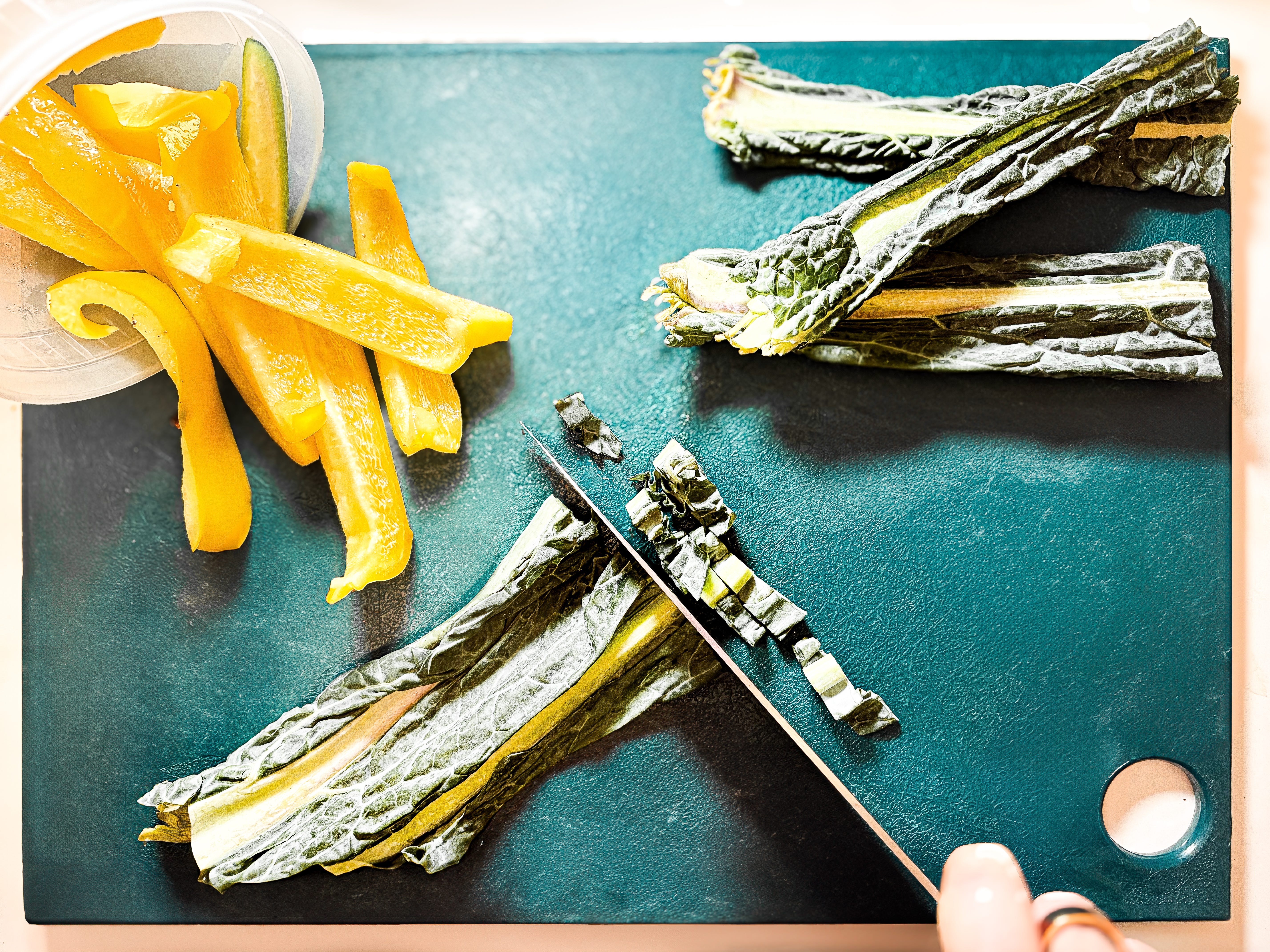 Kale stems and yellow bell peppers on a green cutting board